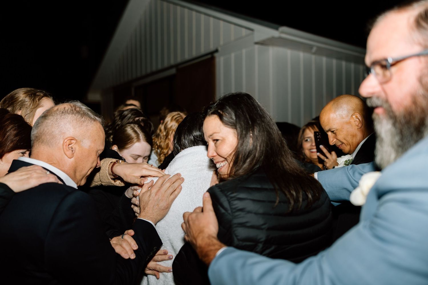 Guests sharing warm embraces and hugs at an outdoor evening wedding celebration.