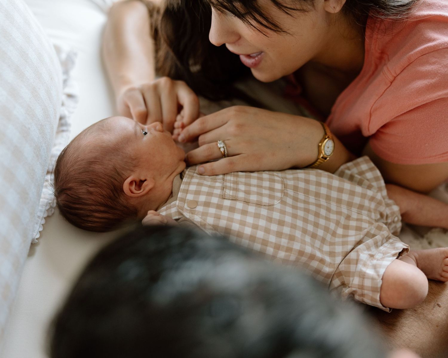 A mother tenderly gazes at her newborn baby lying on a bed, gently touching the infant's face.