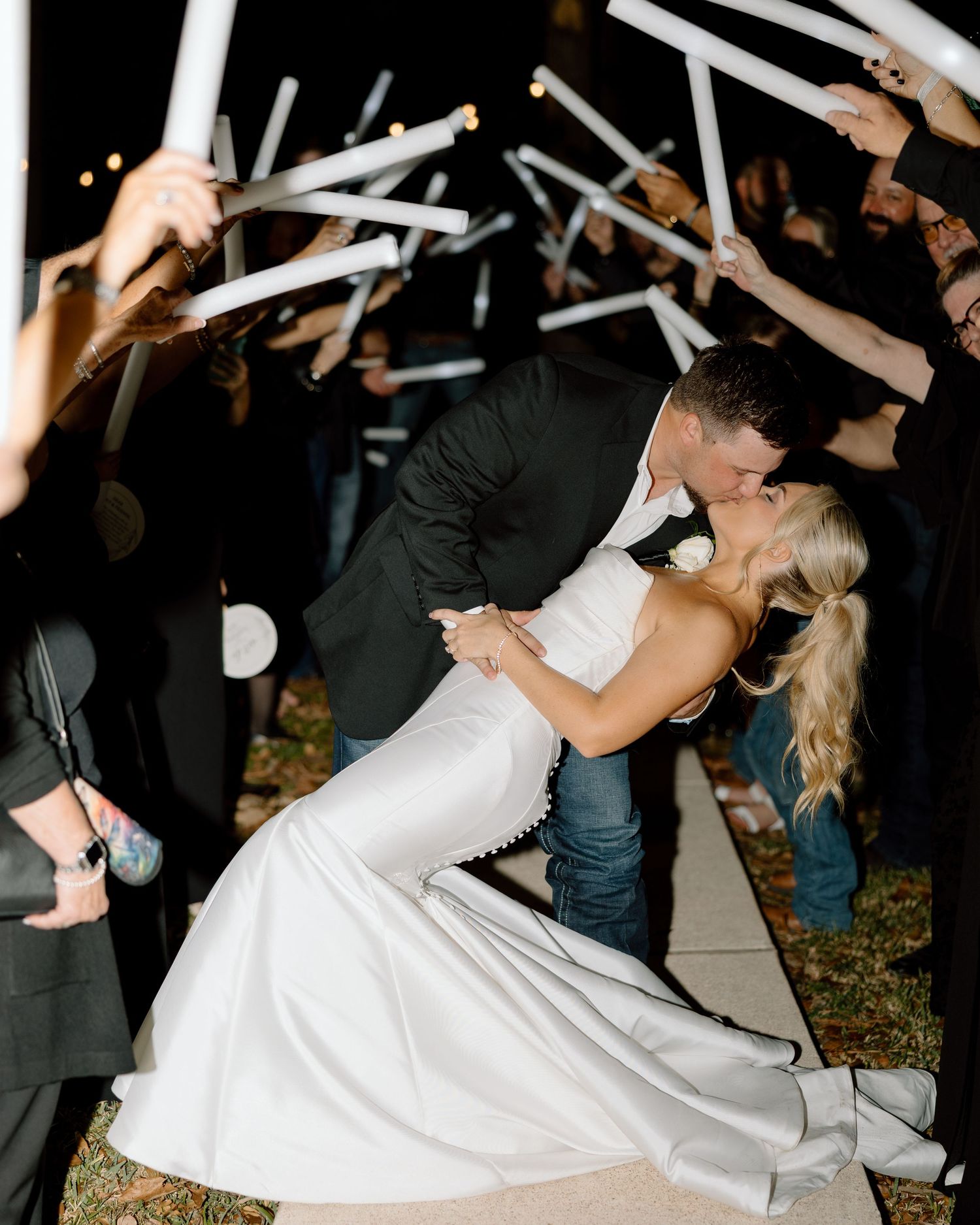 Bride and groom share romantic dip kiss during sparkler send-off exit surrounded by cheering wedding guests.