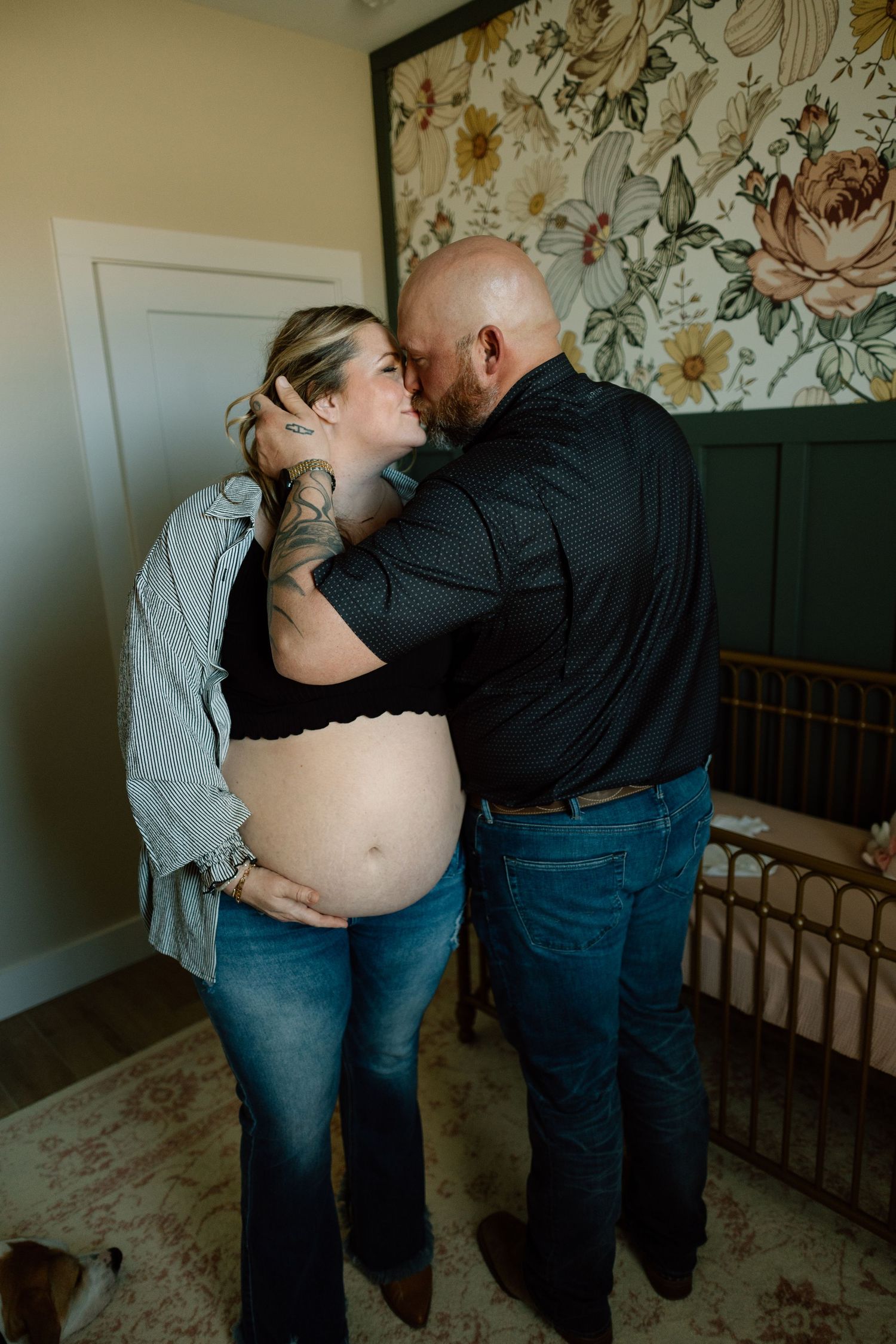 Indoor maternity portrait featuring couple sharing intimate moment against floral wallpaper.