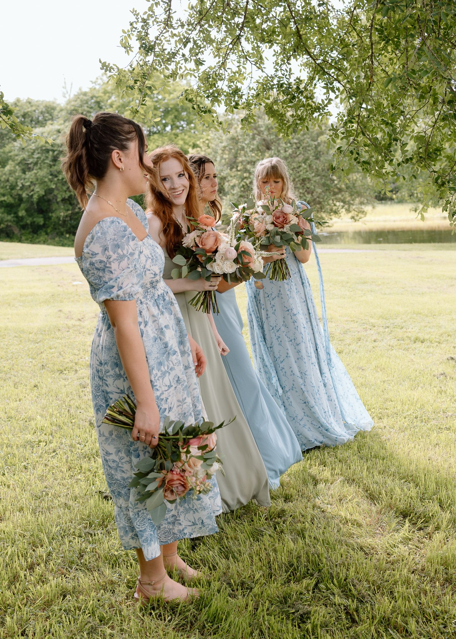 Bridesmaids in light blue dresses holding bouquets pose in a sunny outdoor setting.