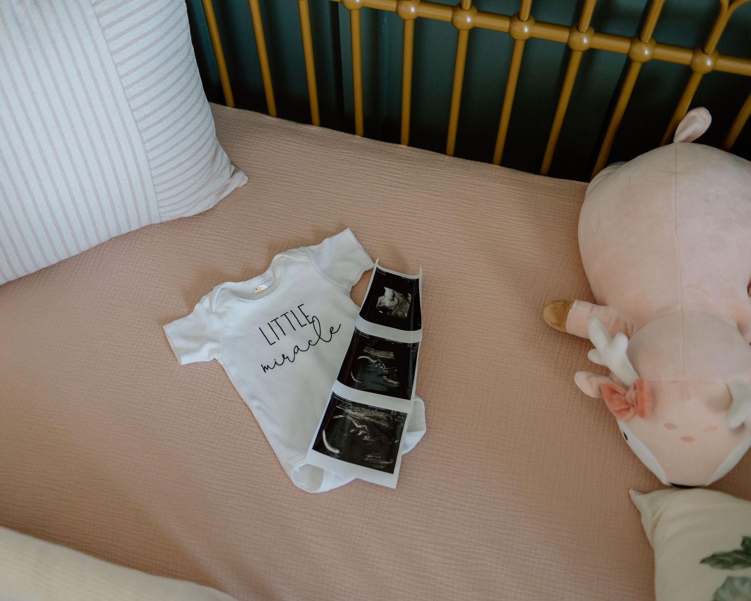Ultrasound photos and a small white onesie displayed in a wooden crib.