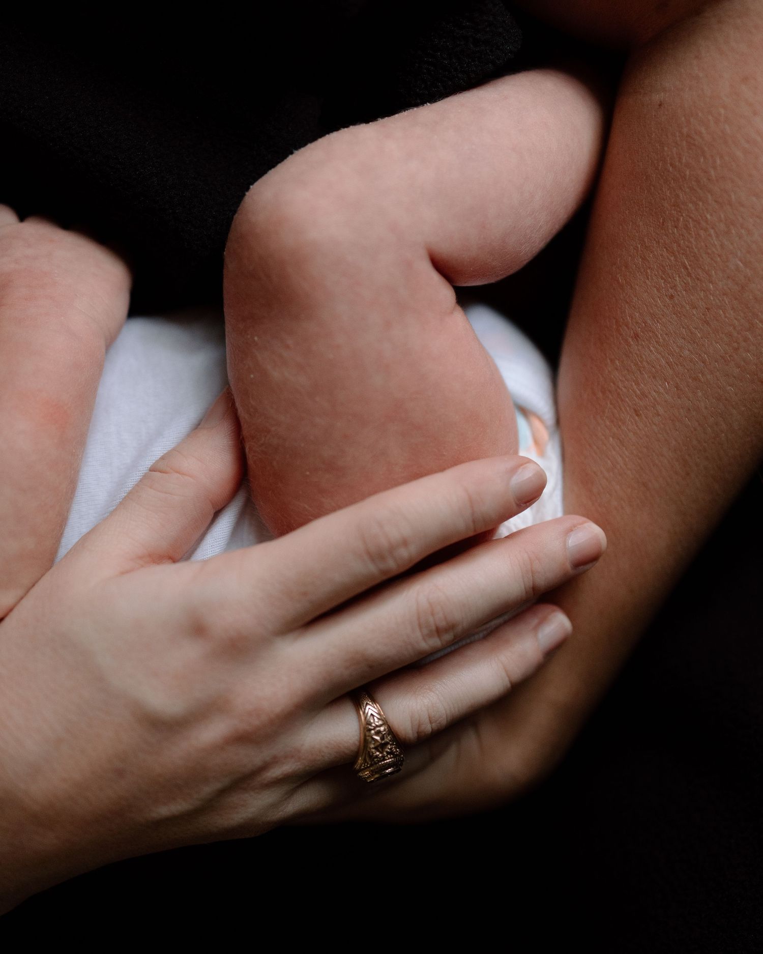 Close up shot of tender hands holding a sleeping newborn baby swaddled in white cloth.