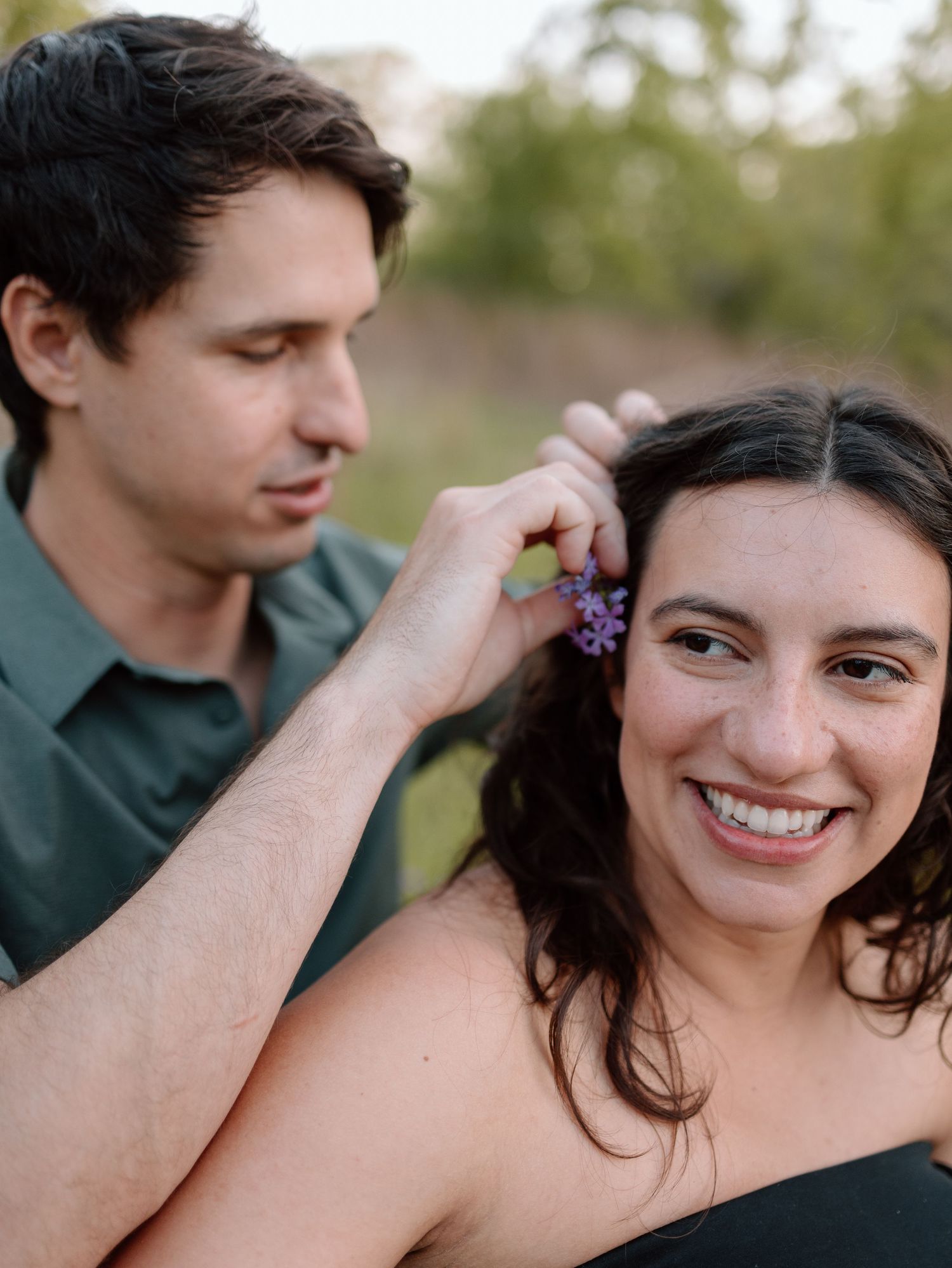 A sweet moment as someone places flowers in dark curly hair outdoors.