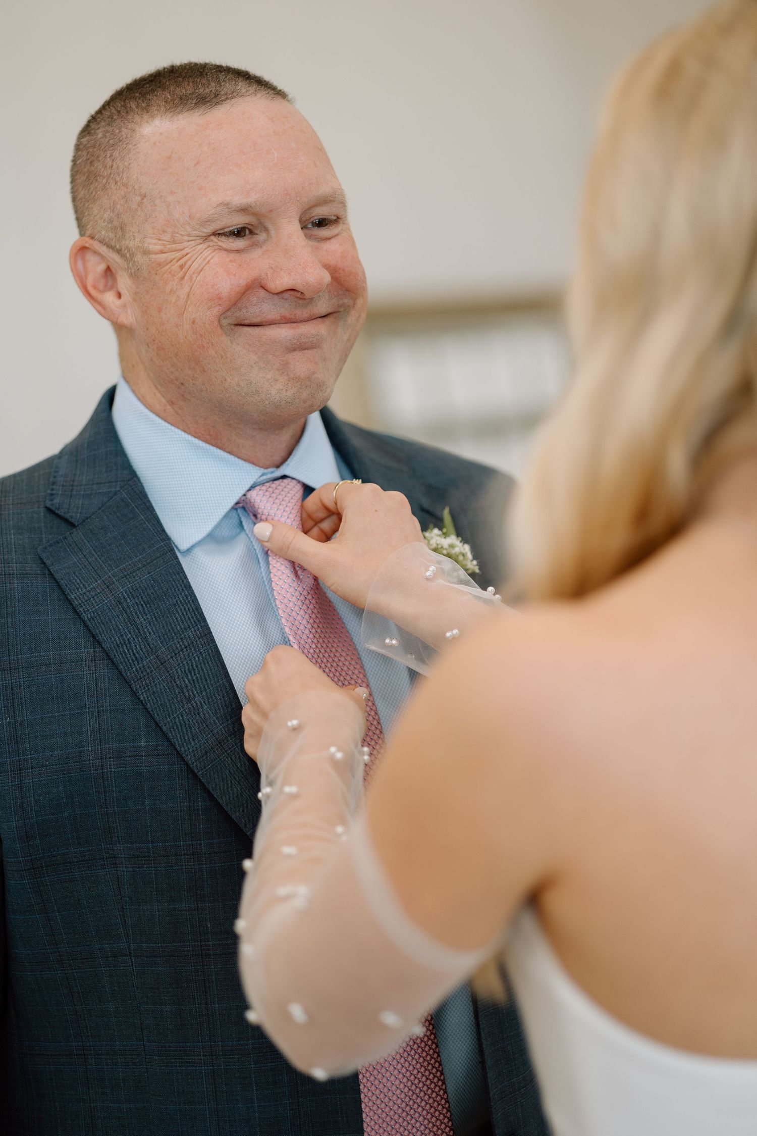 Sweet moment during wedding preparation as boutonniere is pinned to suit.