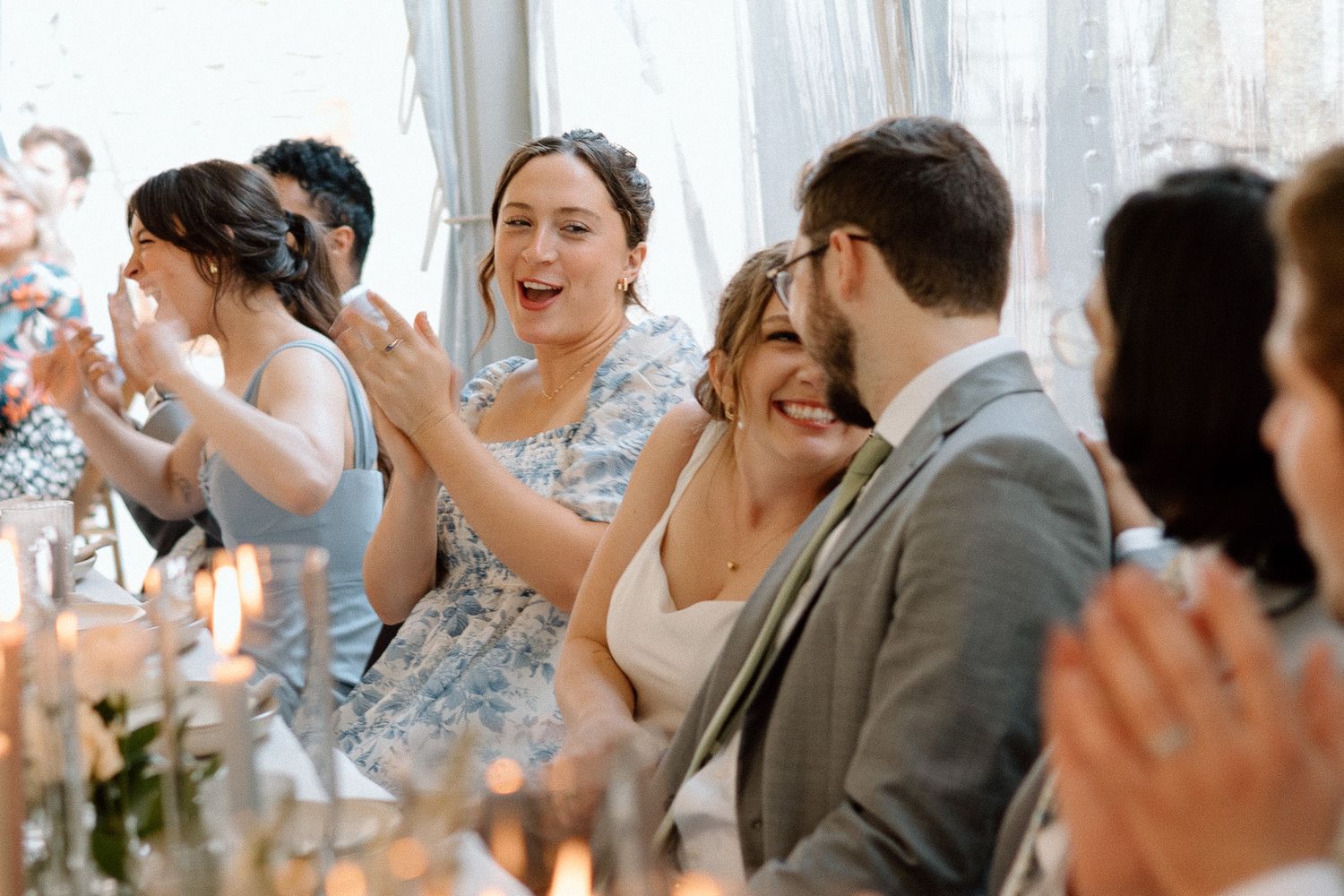 Wedding guests laughing and celebrating during reception dinner under white tent.