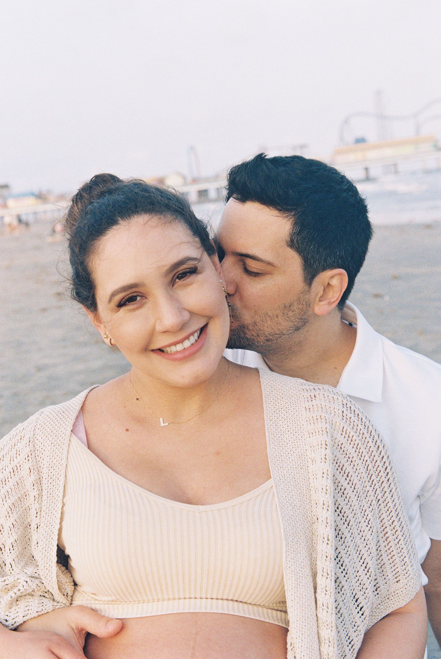 A romantic moment captured at the beach with a couple in casual attire showing affection.