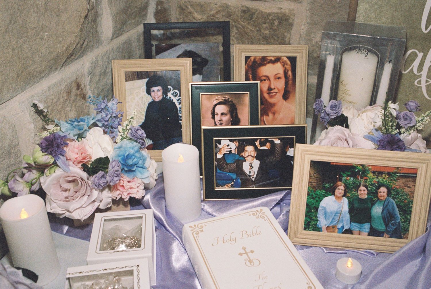 A memorial display with vintage photographs, candles, and blue and purple flowers.
