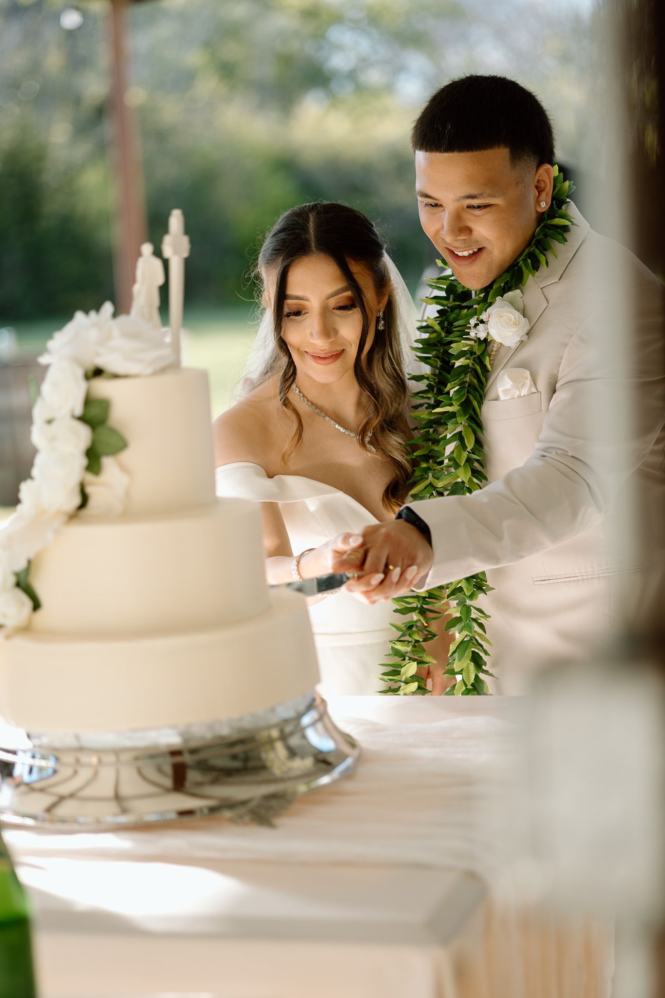 Couple in wedding attire prepare to cut their elegant white tiered wedding cake together.