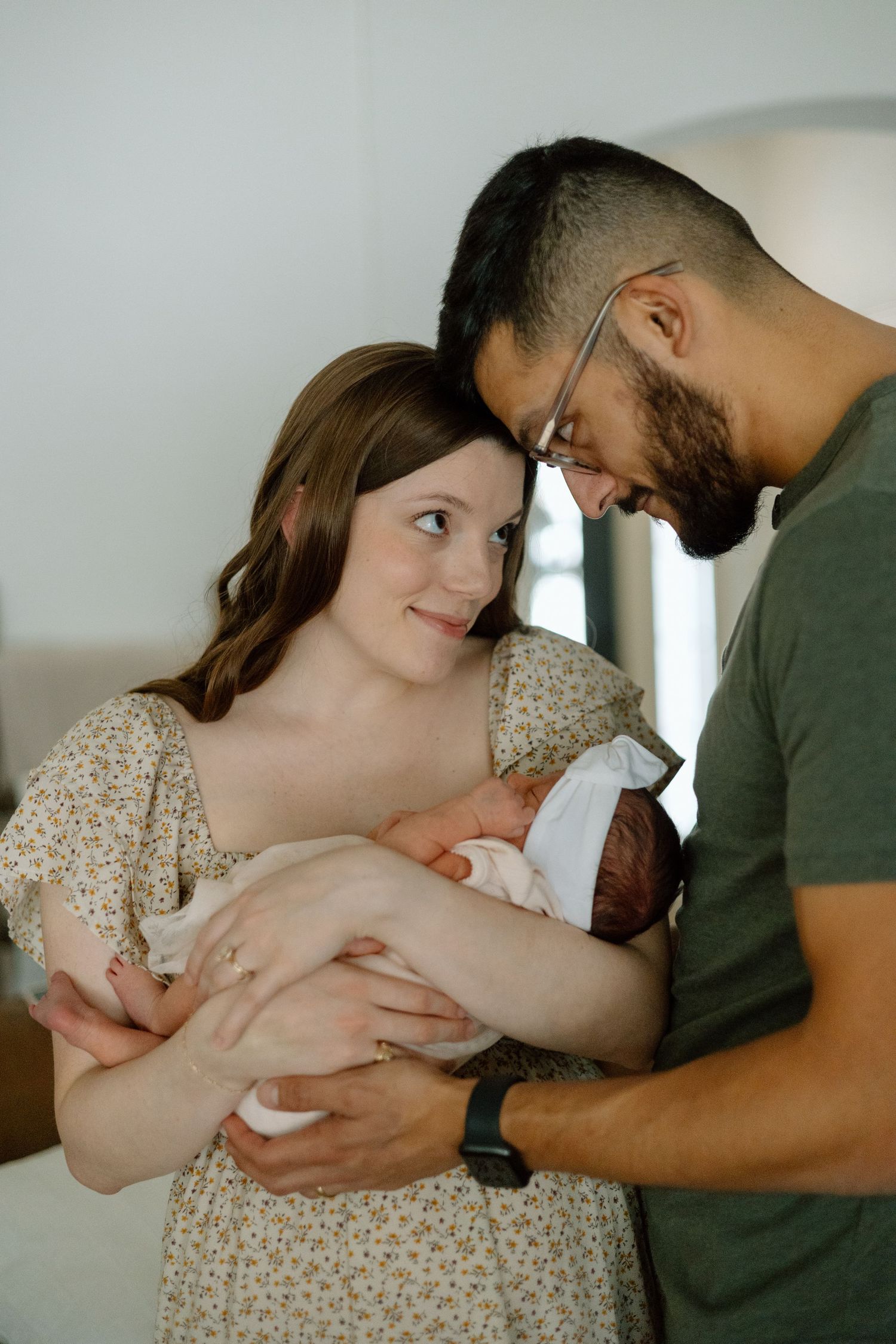 Parents share an intimate moment while holding their newborn in natural light setting.