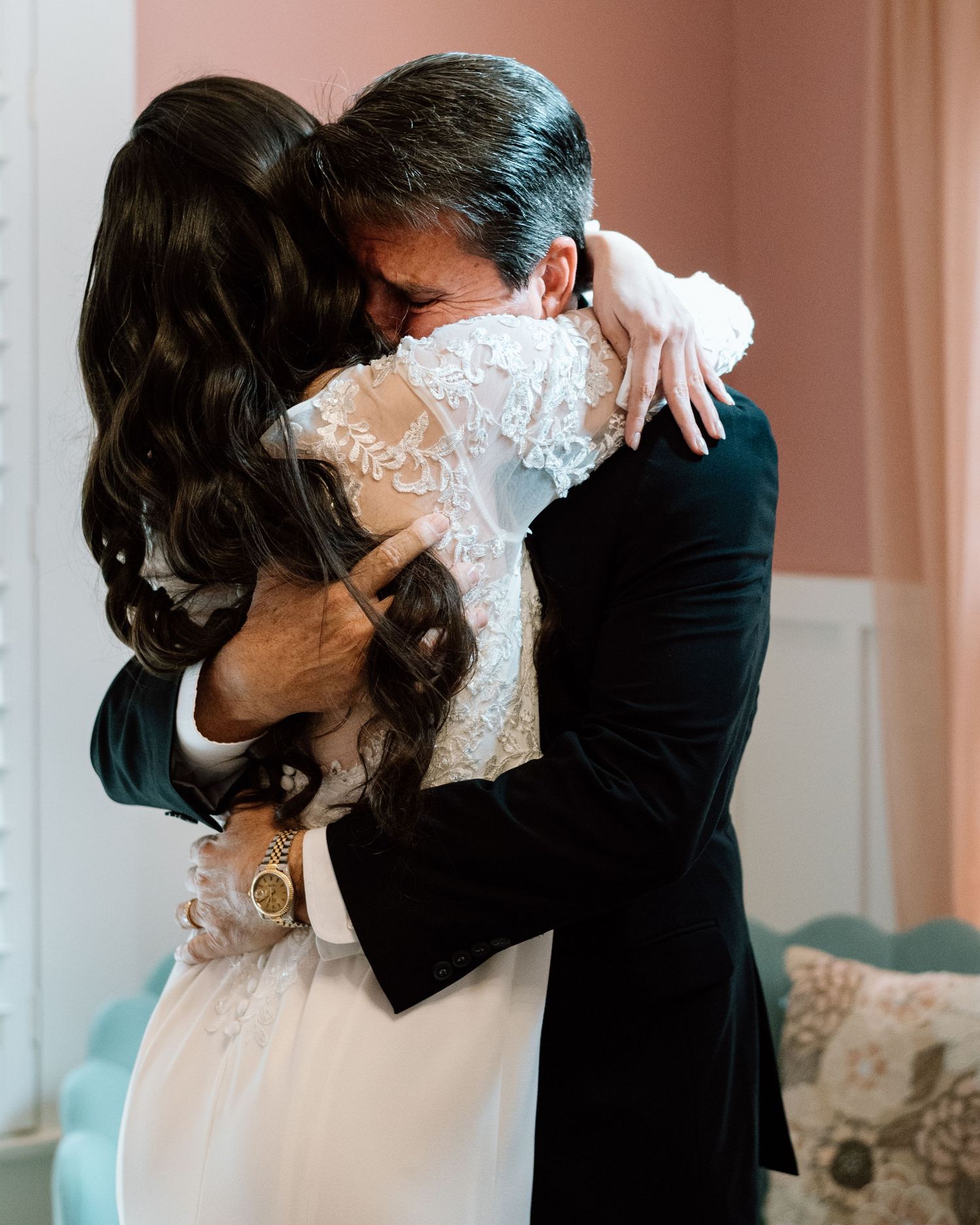 Bride and father sharing an emotional hug during wedding day first look in a softly lit room.