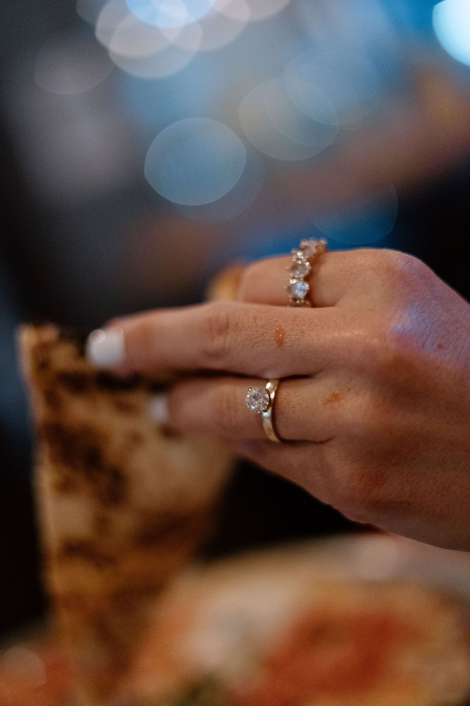 Close-up of a diamond engagement ring and wedding band on a womans finger while holding food.