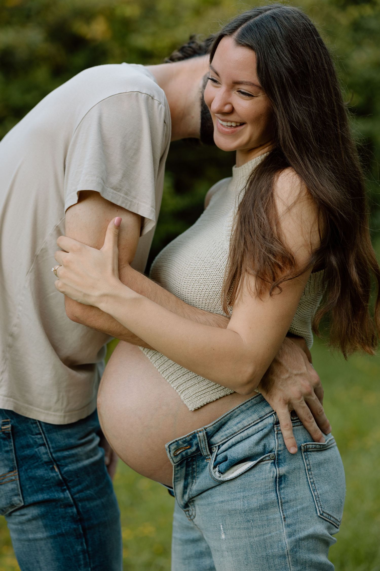 Candid maternity photo of couple sharing intimate moment in garden setting.