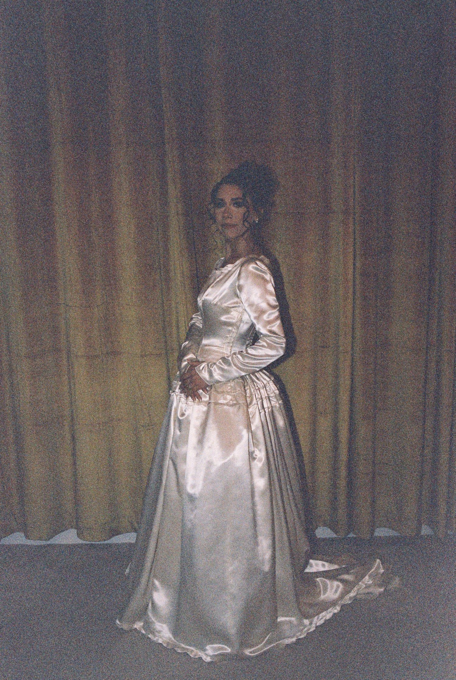 Wedding dress portrait featuring elegant satin gown against golden curtain backdrop.