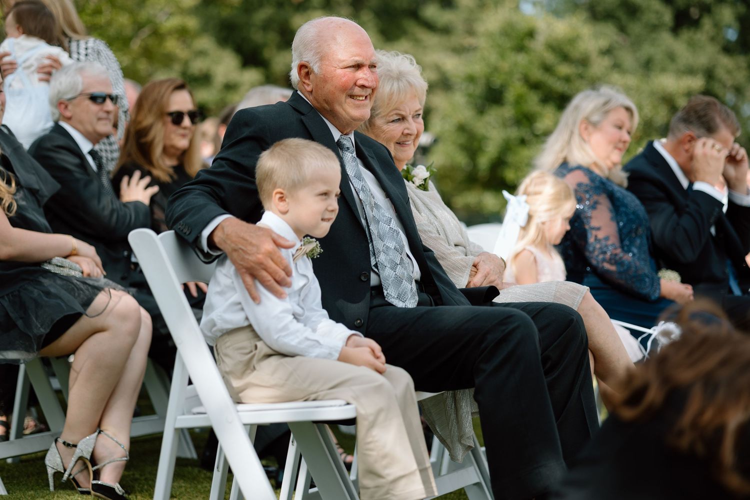 Wedding guests enjoying an outdoor ceremony in white folding chairs.