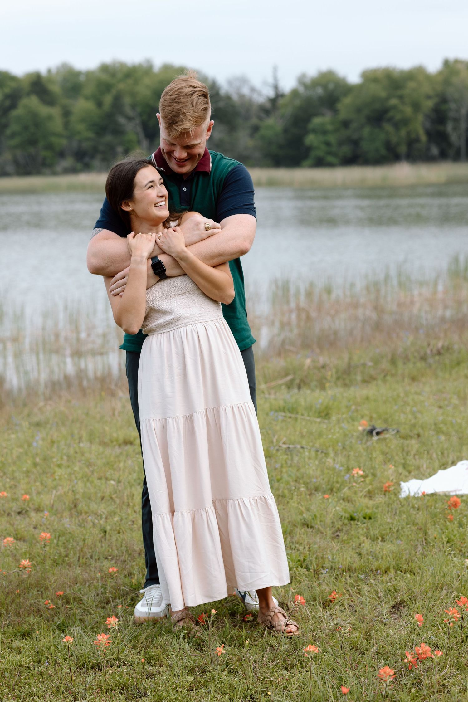 A tender embrace between a couple in a field overlooking a lake.