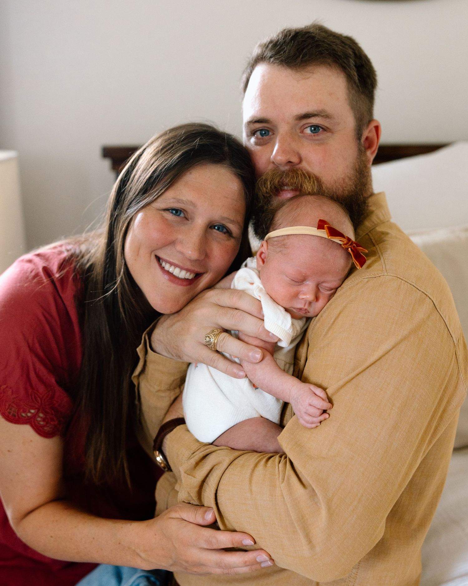 Smiling couple holding their newborn baby, posing together for a family portrait photo.