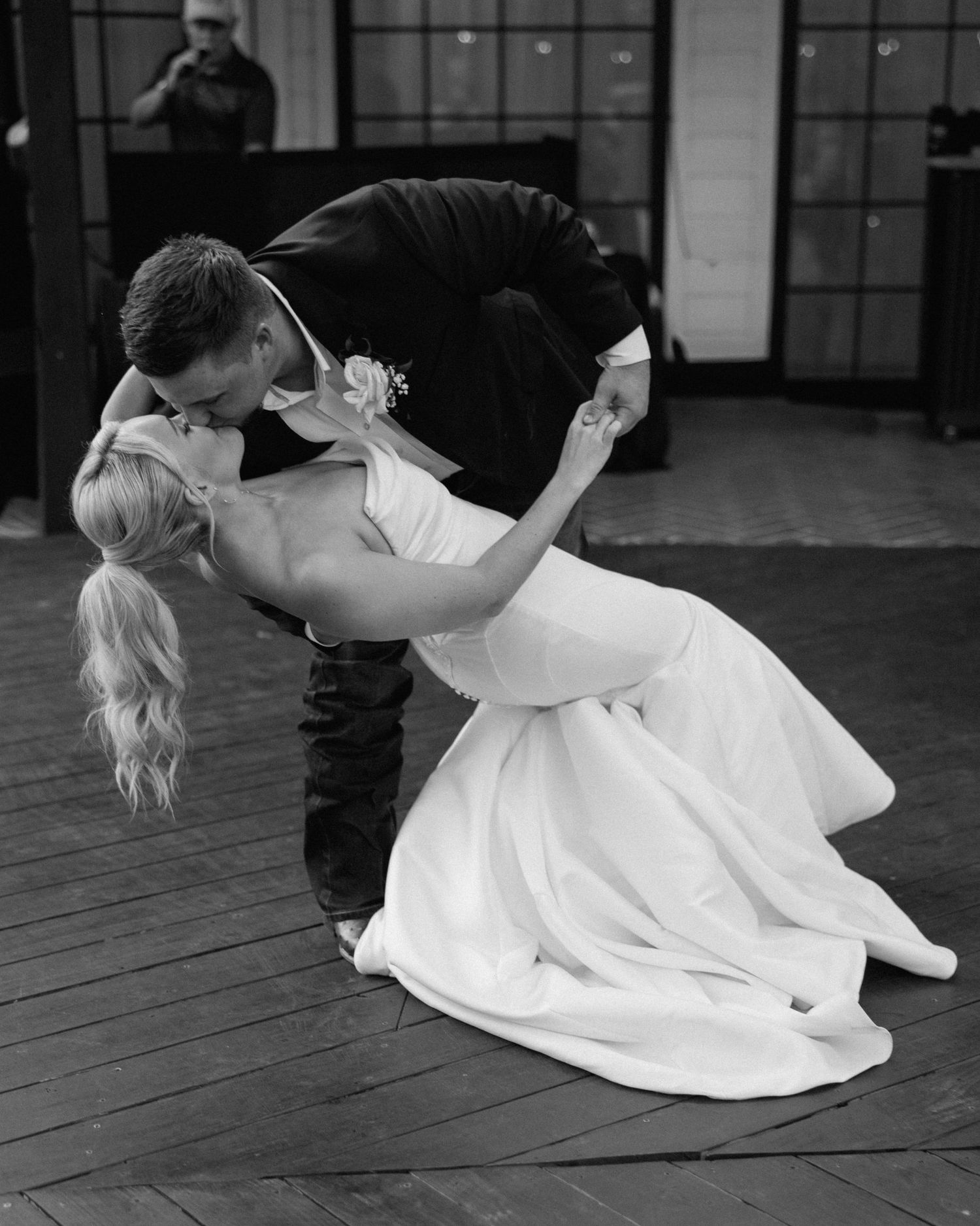 Black and white photo of a groom dipping his bride for a kiss during their first dance at a wedding reception.