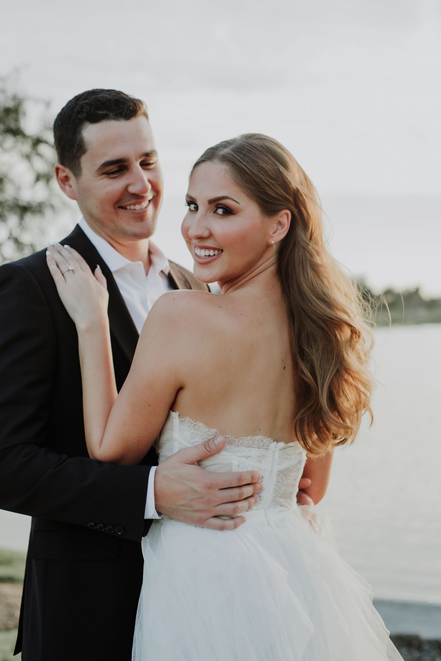 A romantic wedding portrait of a couple in formal attire against a cloudy sky.