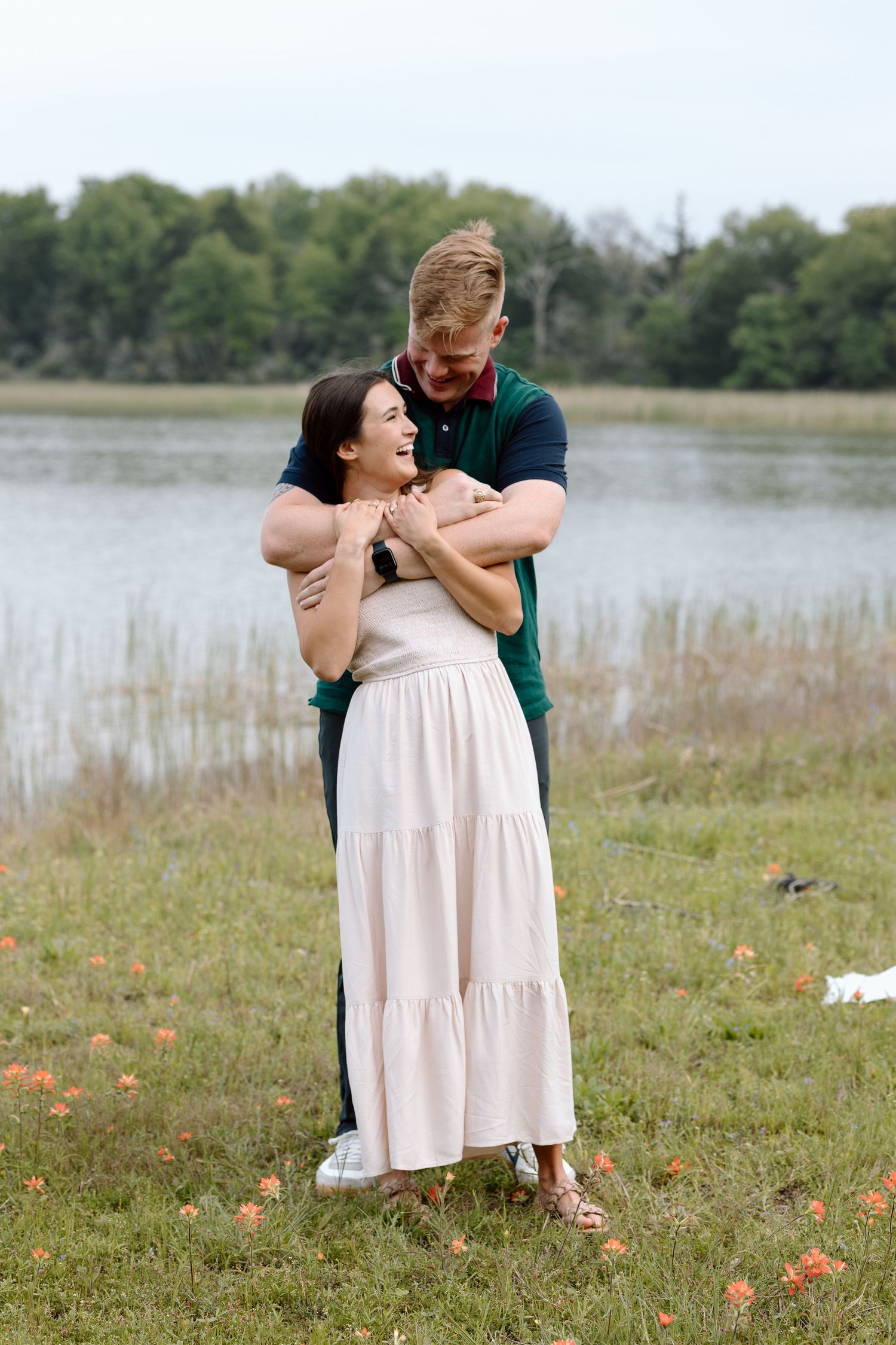 A couple shares a loving embrace while standing in a field by a lake.