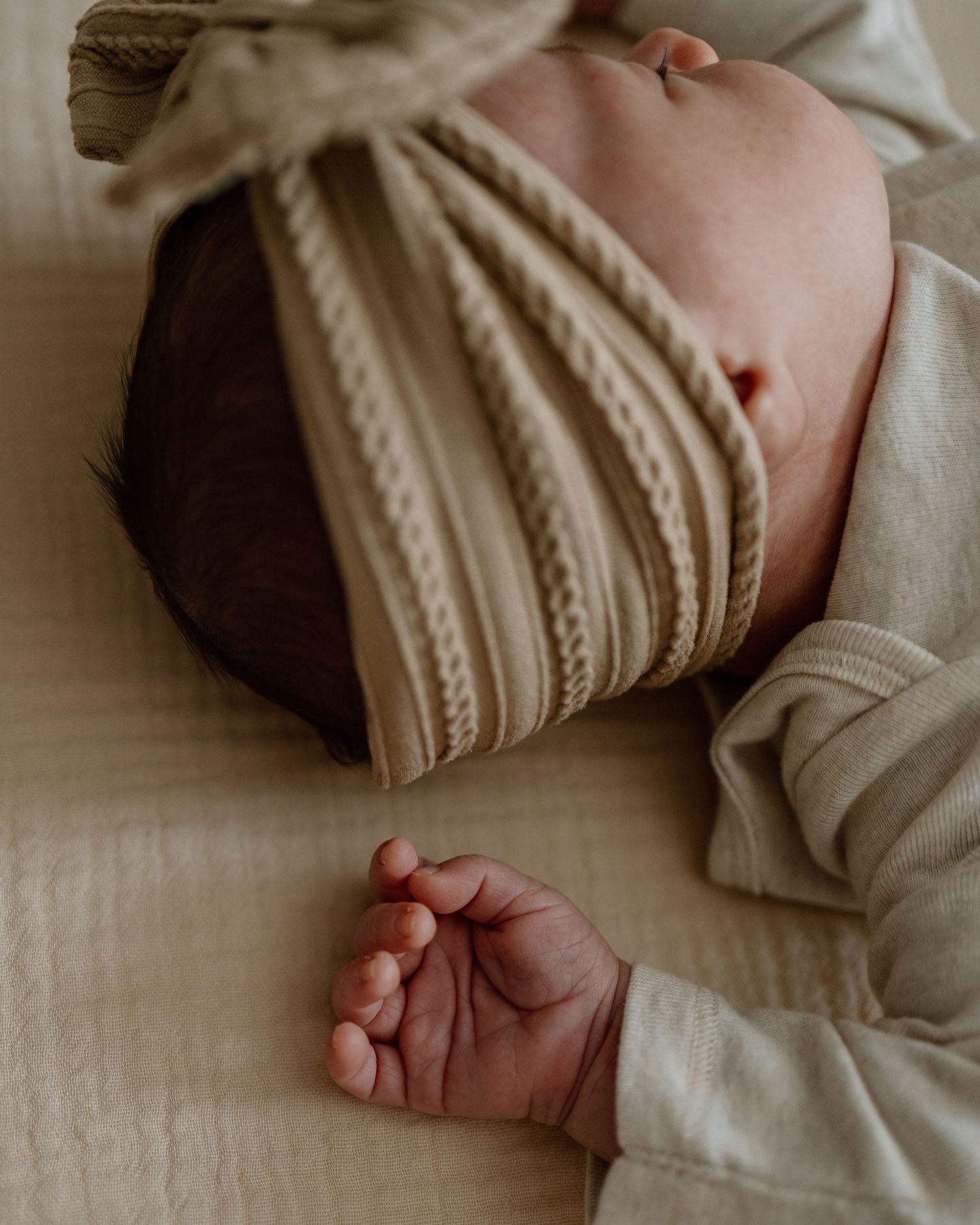 Close-up of a sleeping baby wearing a knitted beige bow headband.