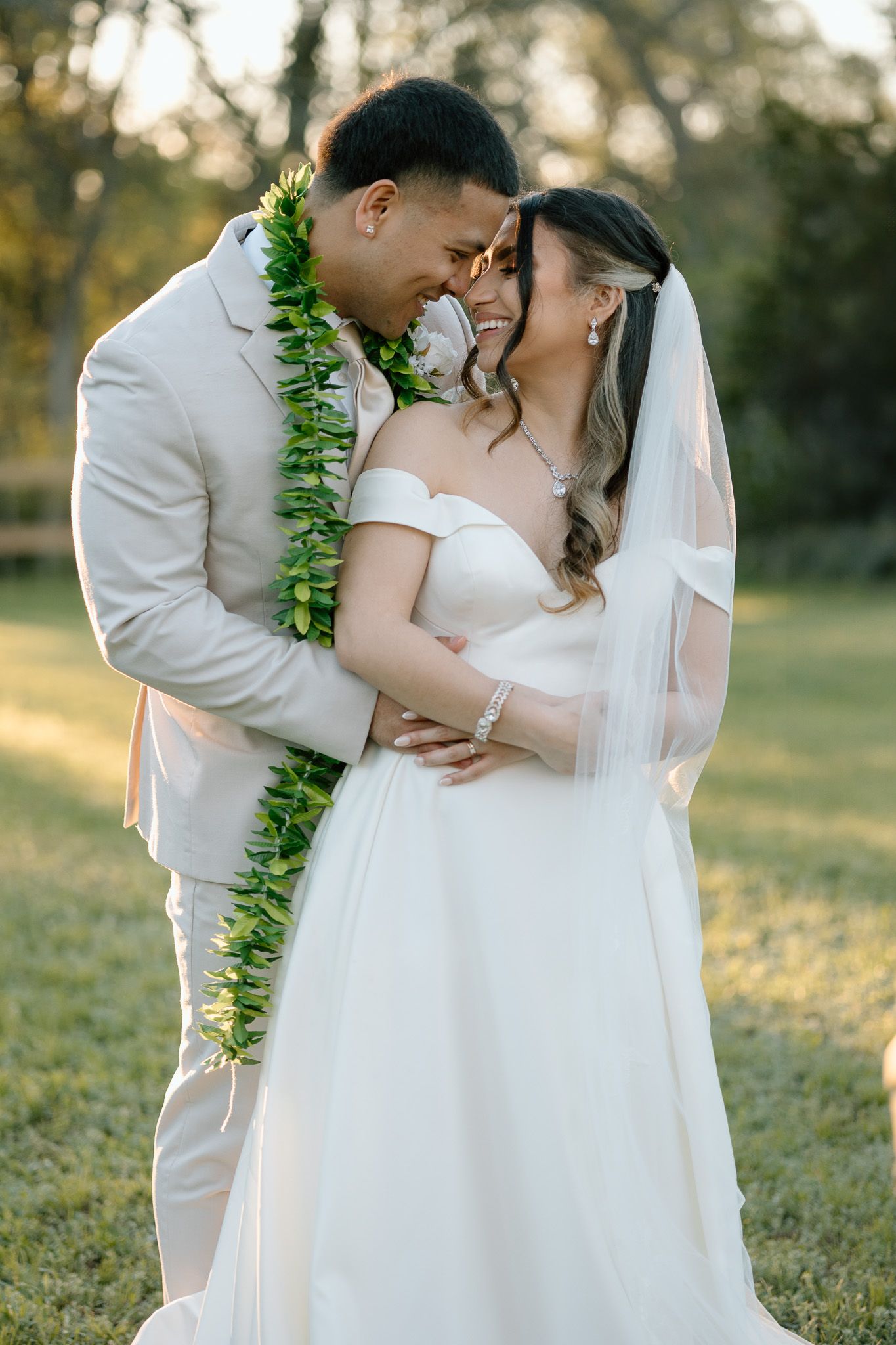 A tender moment between newlyweds wearing traditional Hawaiian lei and wedding attire in golden sunlight.