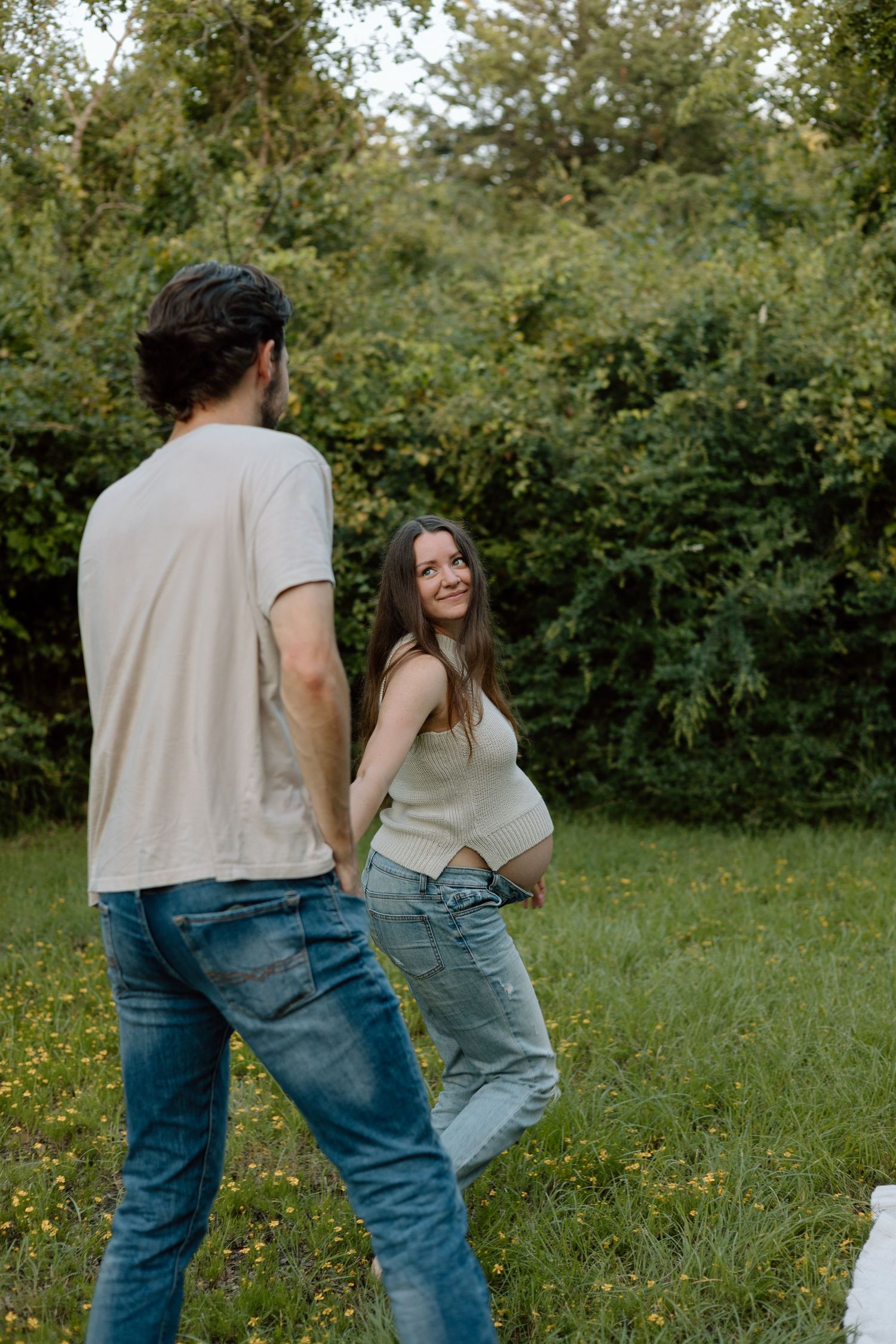A playful maternity photo of a couple in casual clothes outdoors.