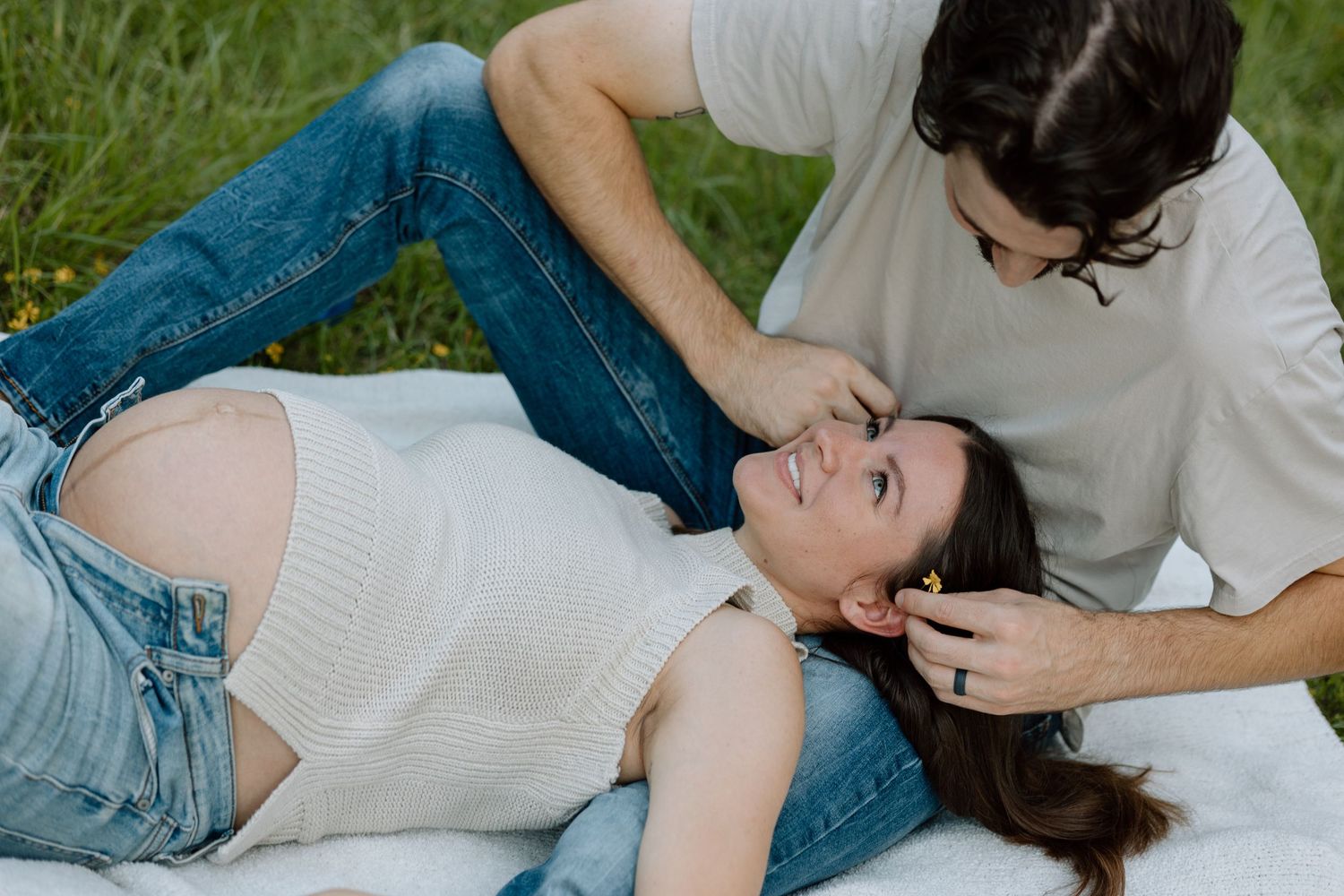 Intimate outdoor maternity photo with couple laying in grass wearing casual clothes.