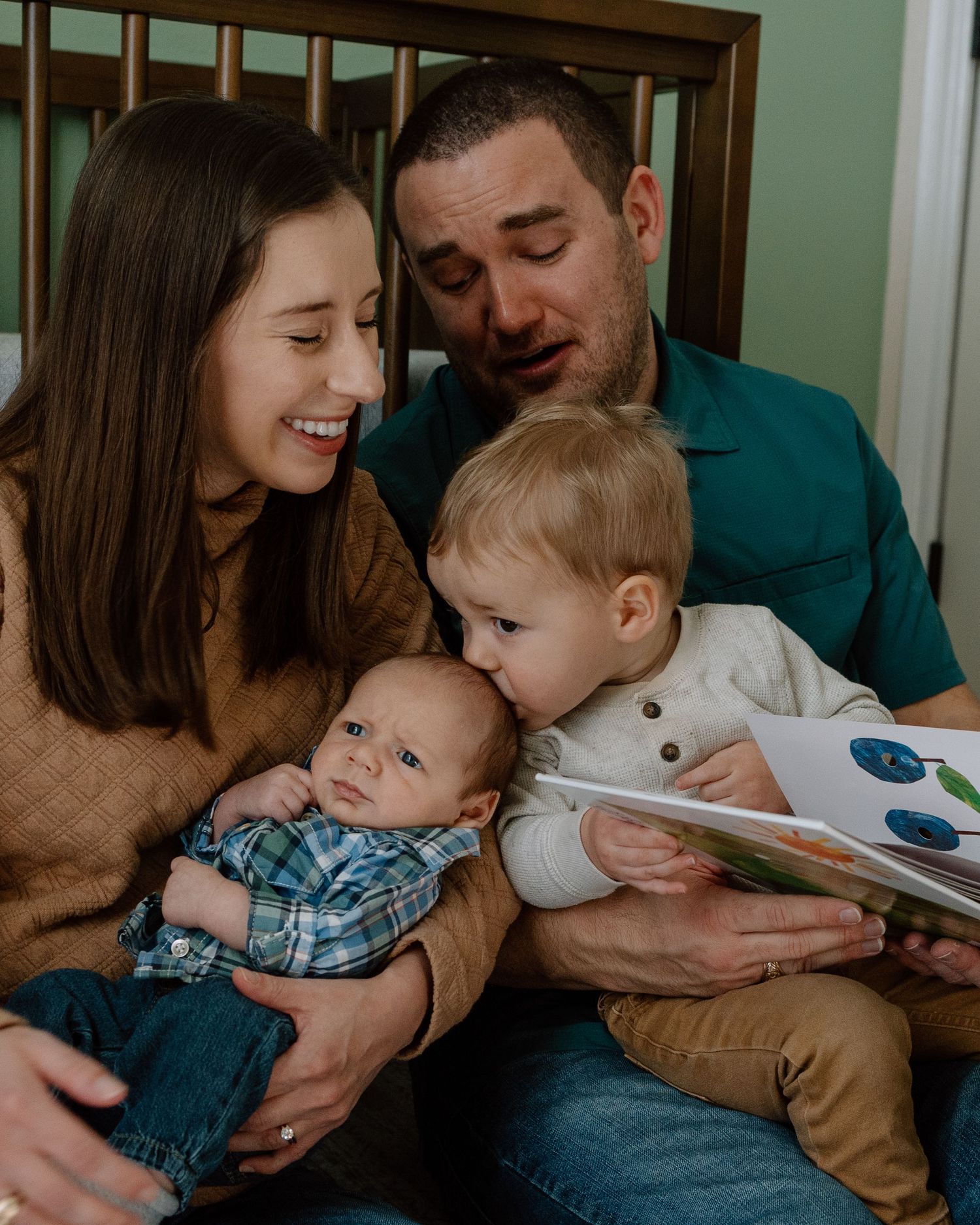 A cozy family moment sharing a book together on a bed with wooden headboard.