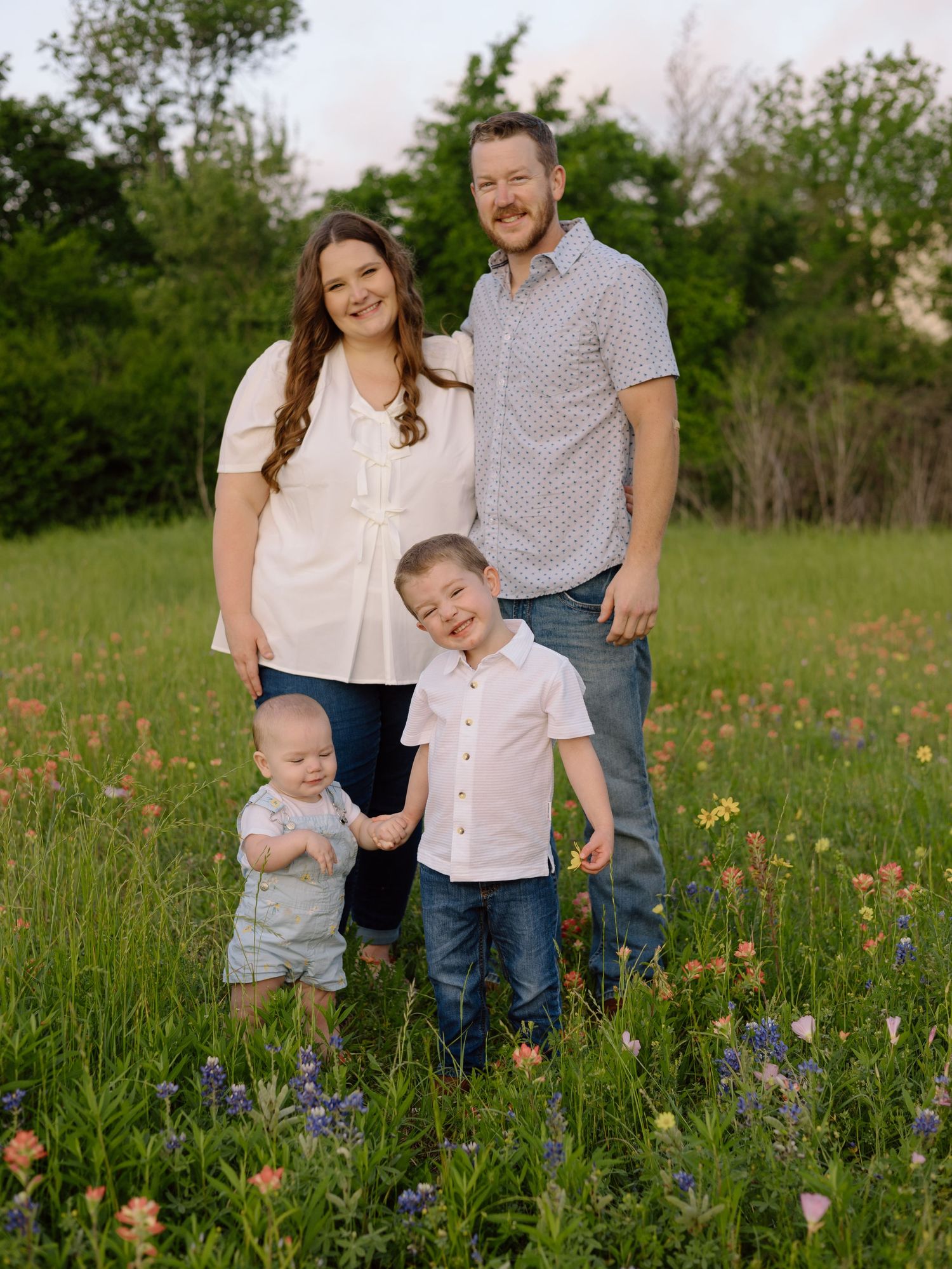 A family wearing coordinated casual outfits poses together in a wildflower meadow during spring.