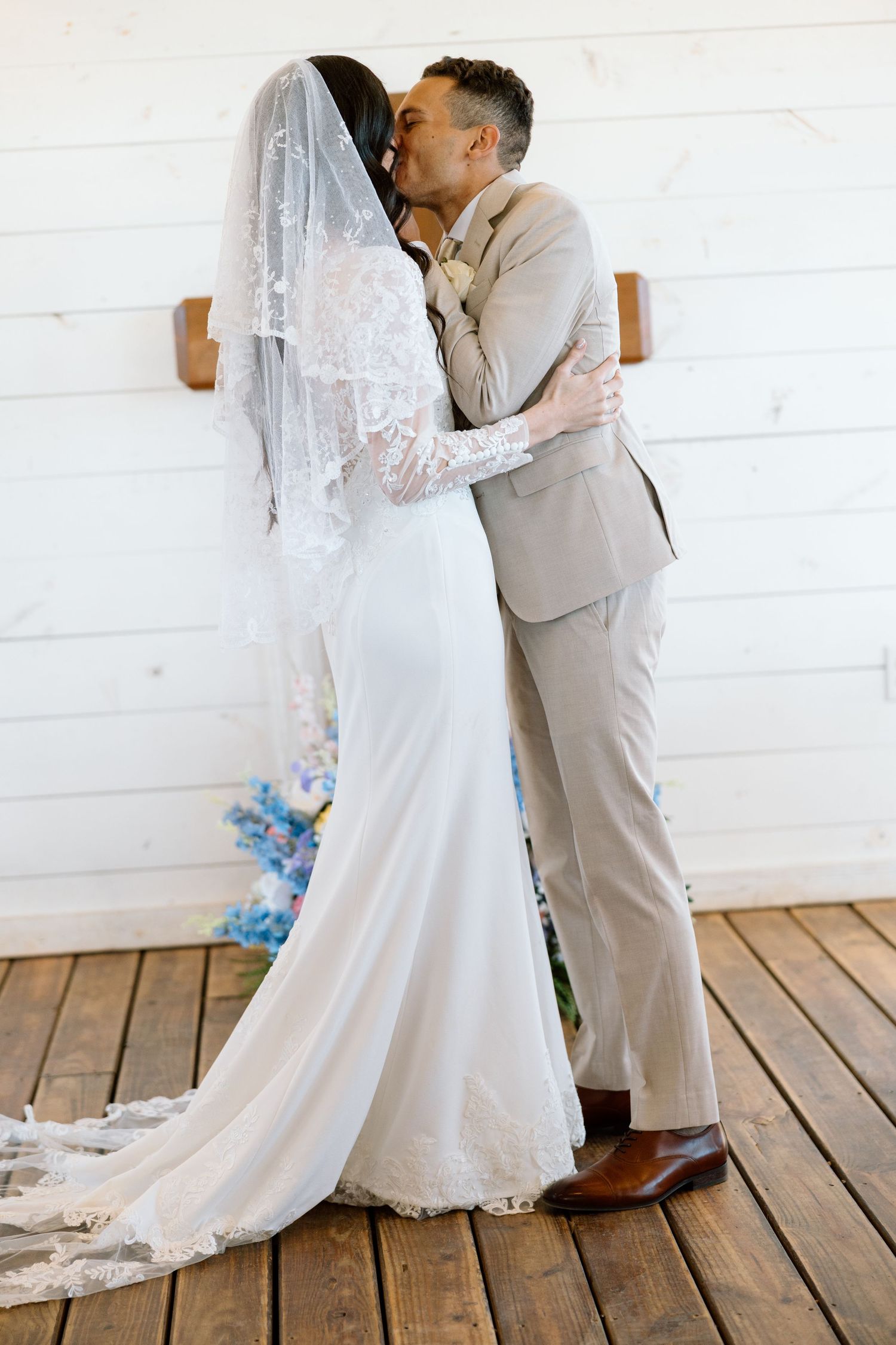 Bride and groom sharing first kiss at rustic barn wedding ceremony.