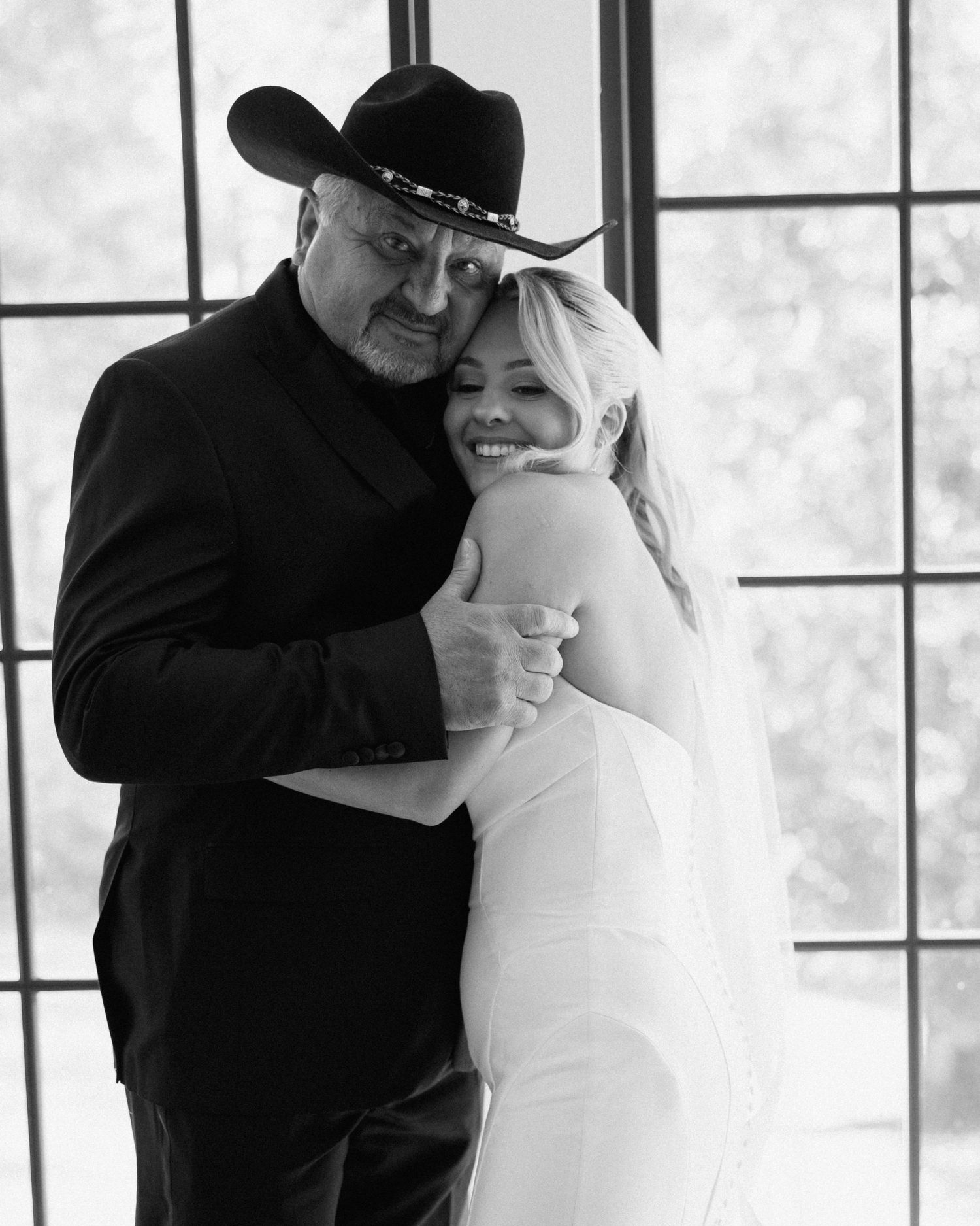Black and white photo of a couple embracing, man in cowboy hat and suit, woman in white wedding dress.