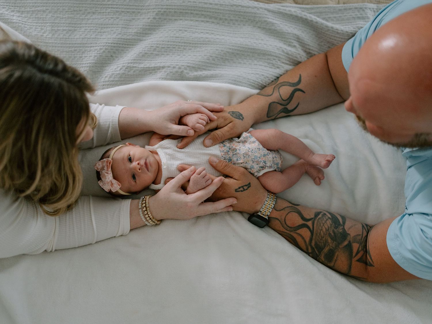 A bright, playful moment of relaxation and joy captured in bed with visible tattoos and light bedding.