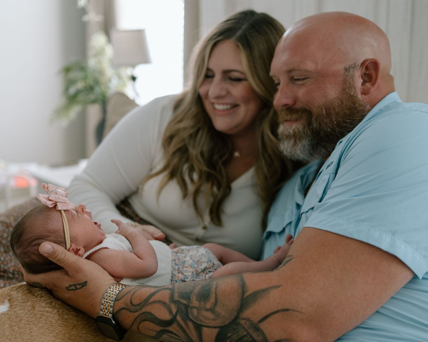Loving couple sitting together on couch cuddles with their newborn baby in a bright, comfortable setting.