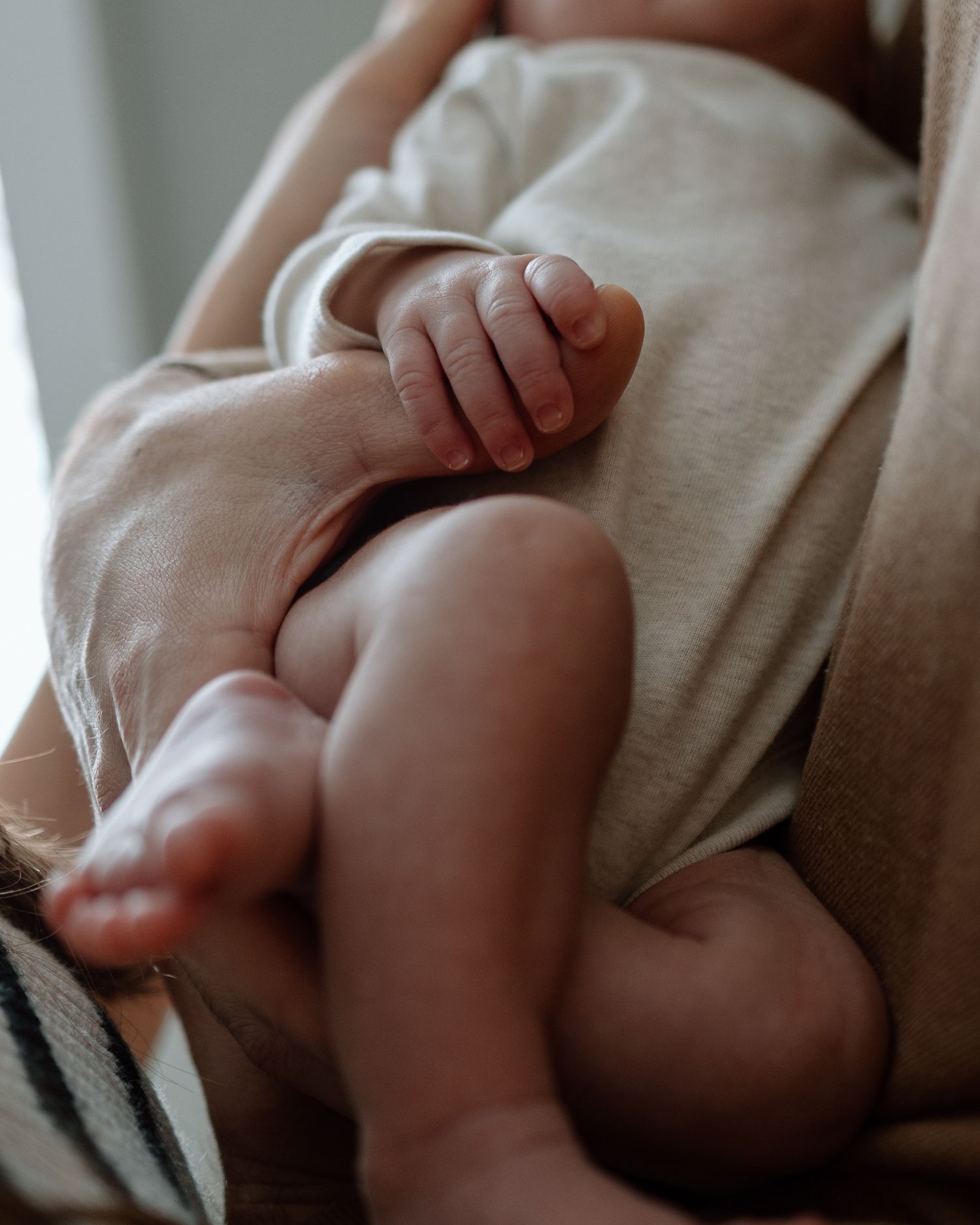 Close-up of tiny newborn baby's hand and leg against soft neutral fabric.
