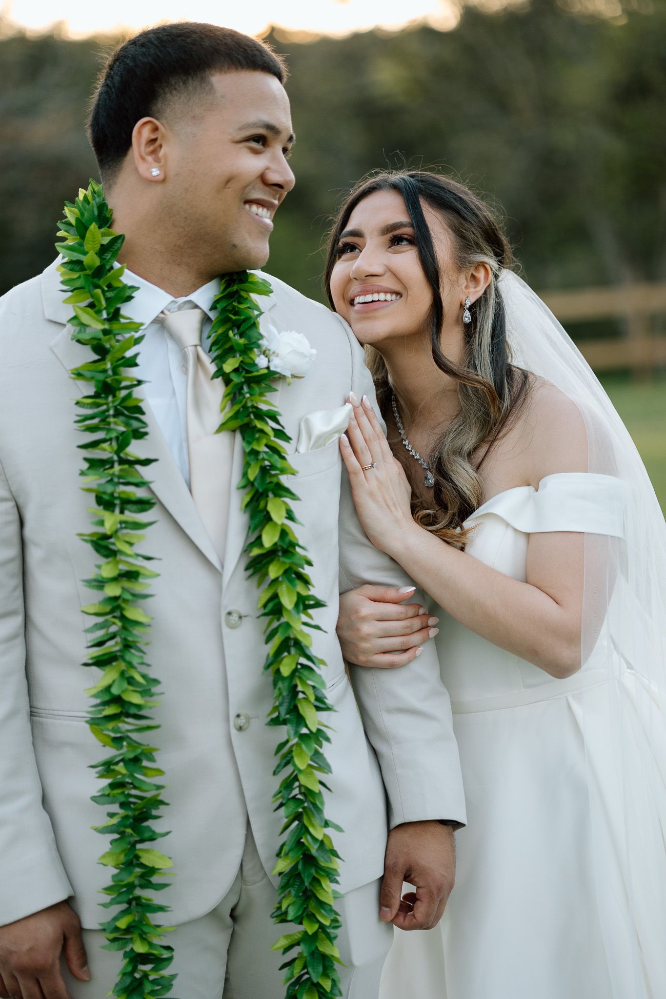 Wedding couple sharing a joyful moment while wearing traditional Hawaiian maile lei and formal attire.
