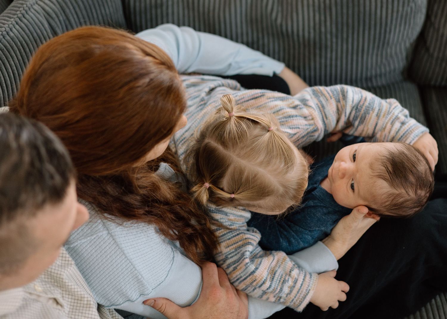 A mother with red hair cuddles two young children on a gray sofa in a warm family moment.