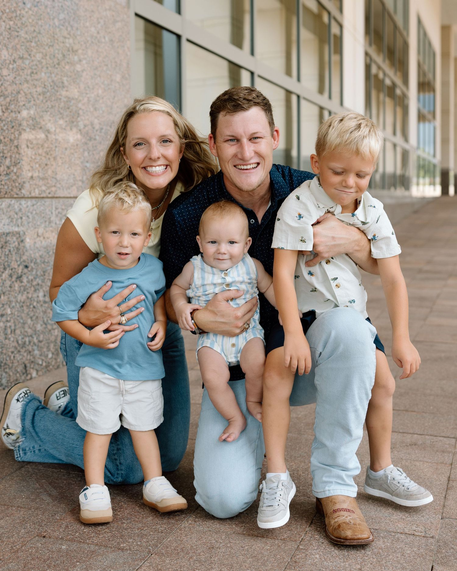 Young family of five smiling together outdoors, parents with three small children including a baby.