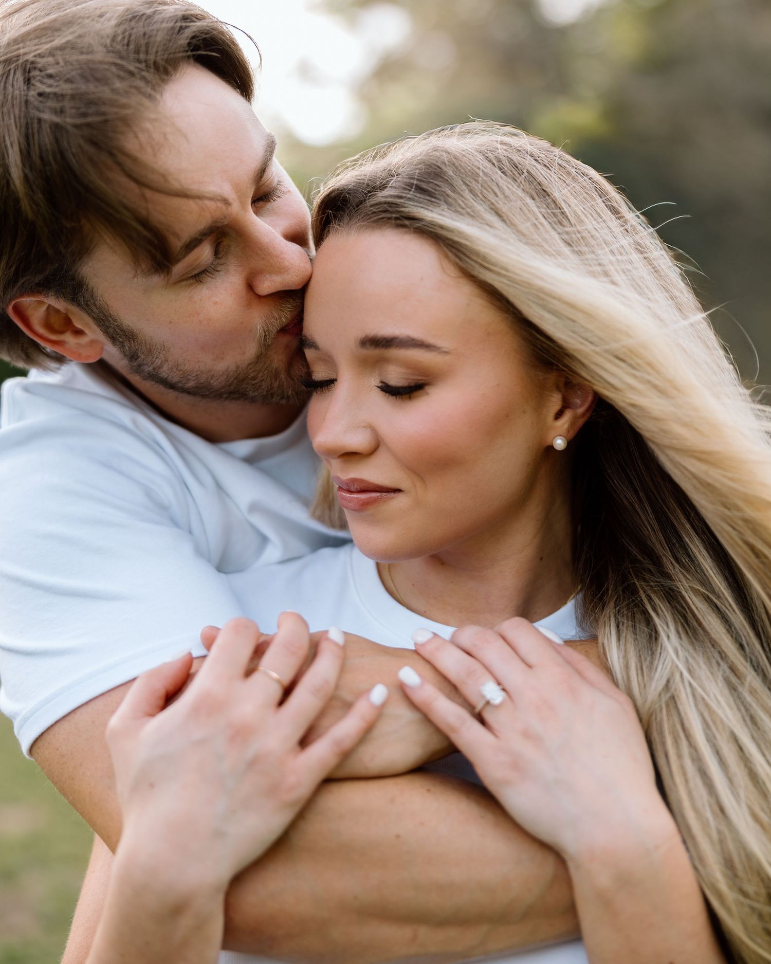 Romantic couple embracing outdoors, man kissing woman's temple while holding her close in a tender moment.