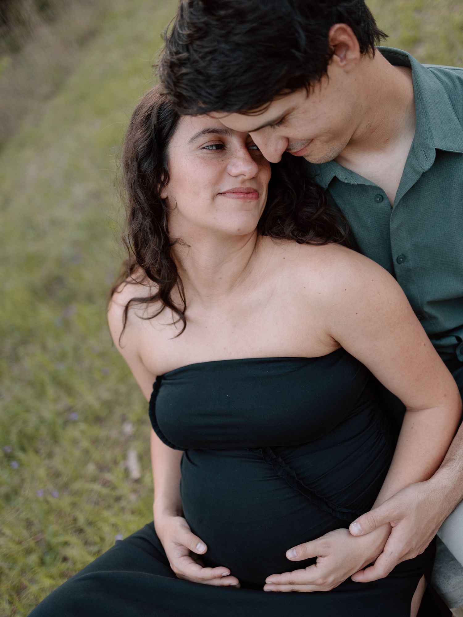 Intimate maternity portrait of couple embracing in an outdoor setting with natural lighting.