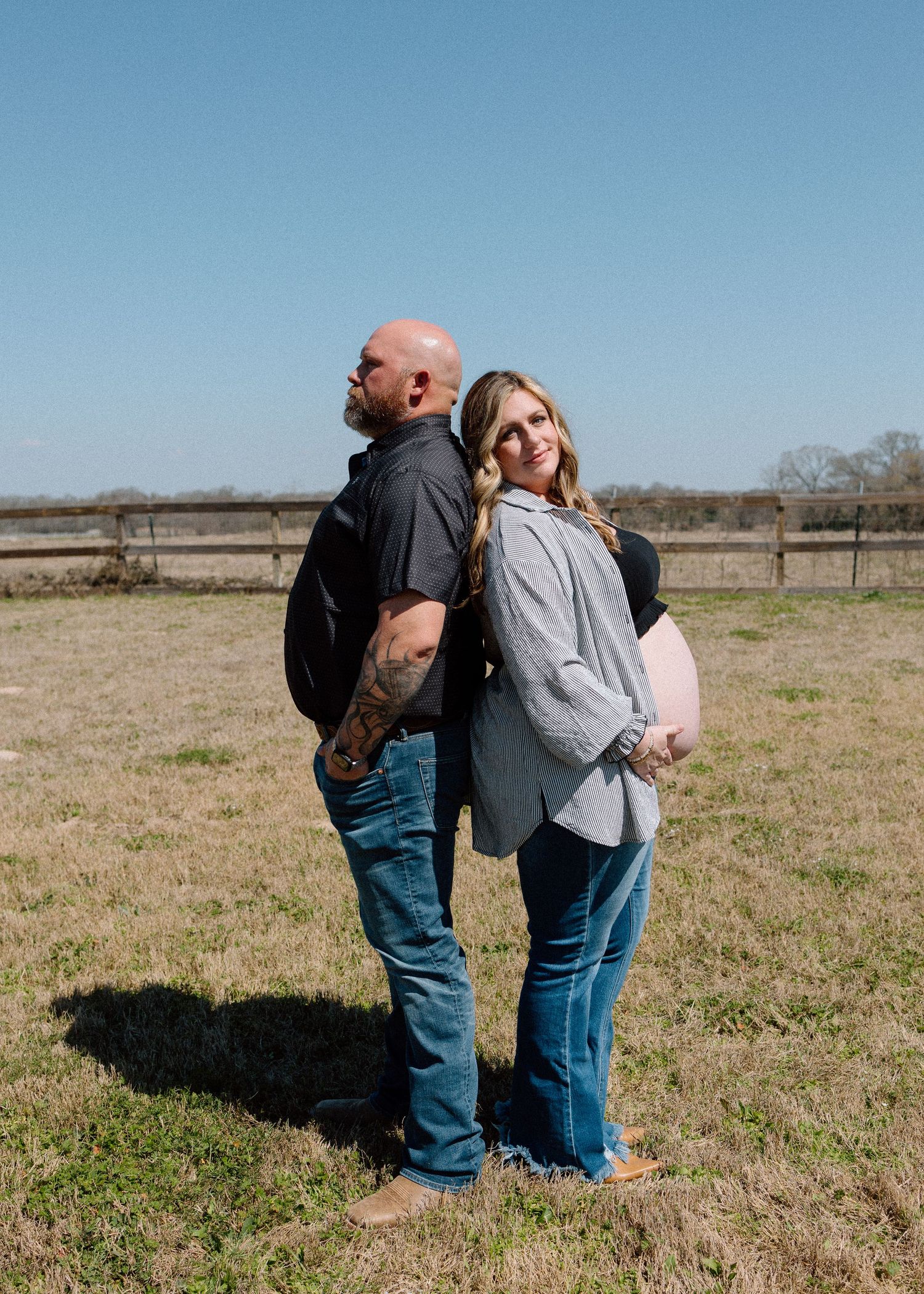 Casual outdoor maternity portrait of couple standing back-to-back in field.