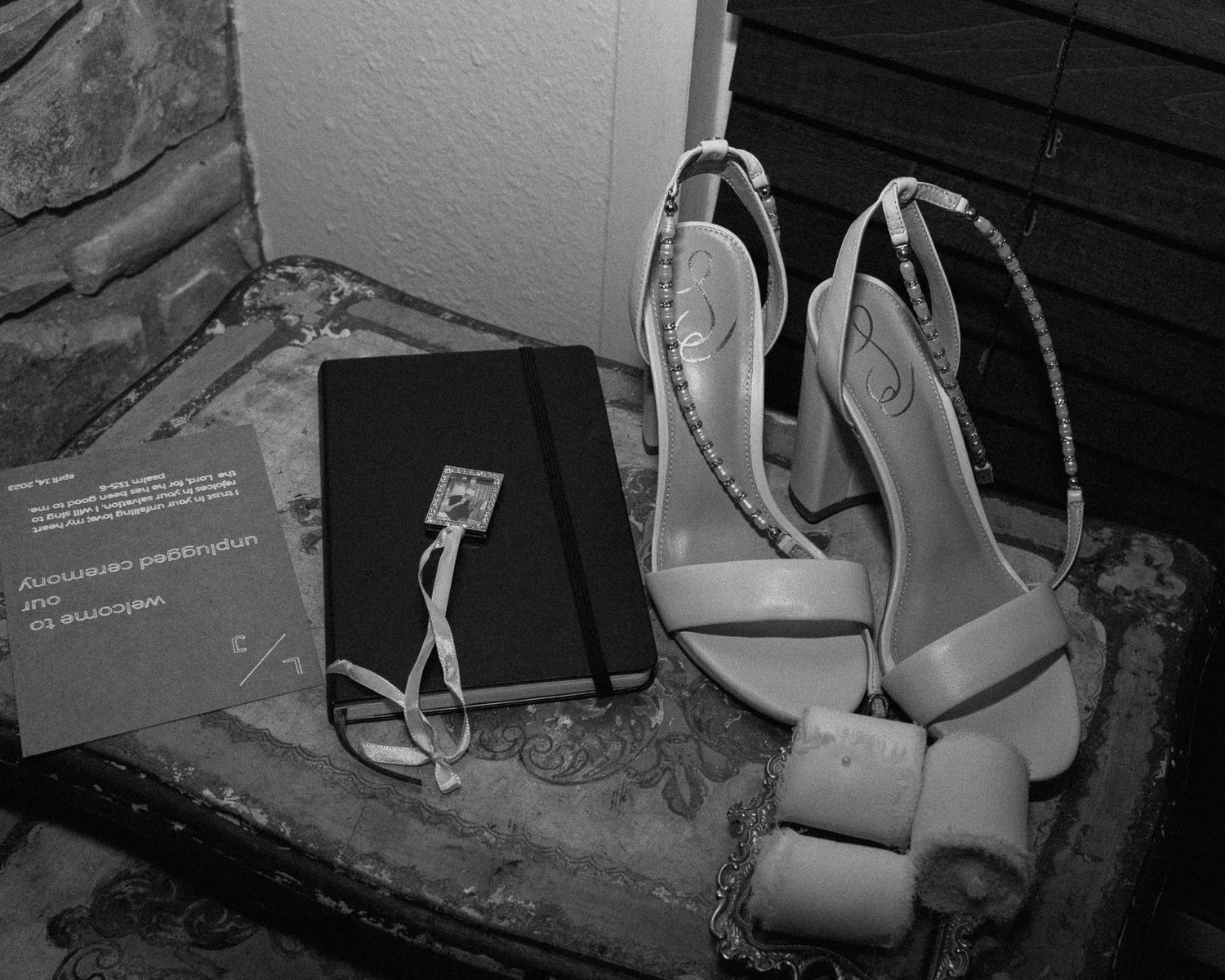 Wedding accessories including shoes and a dark book arranged in black and white photography.