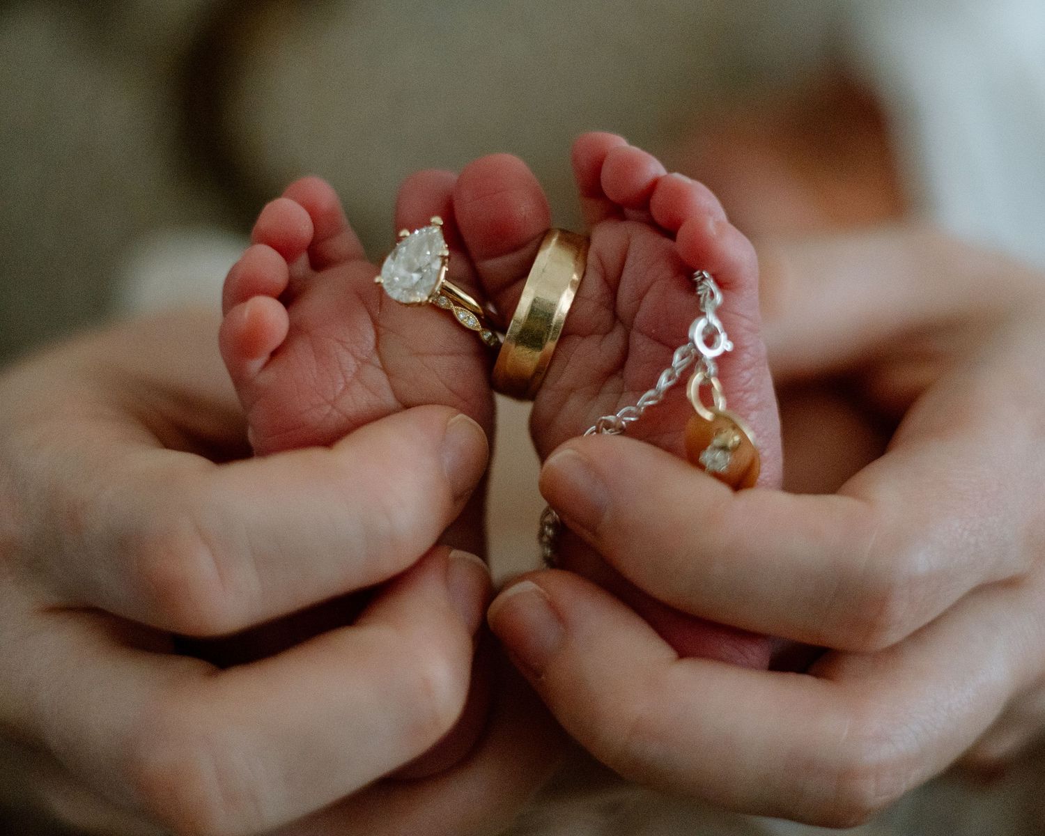 Close-up shot of tiny baby feet nestled between hands adorned with elegant rings.