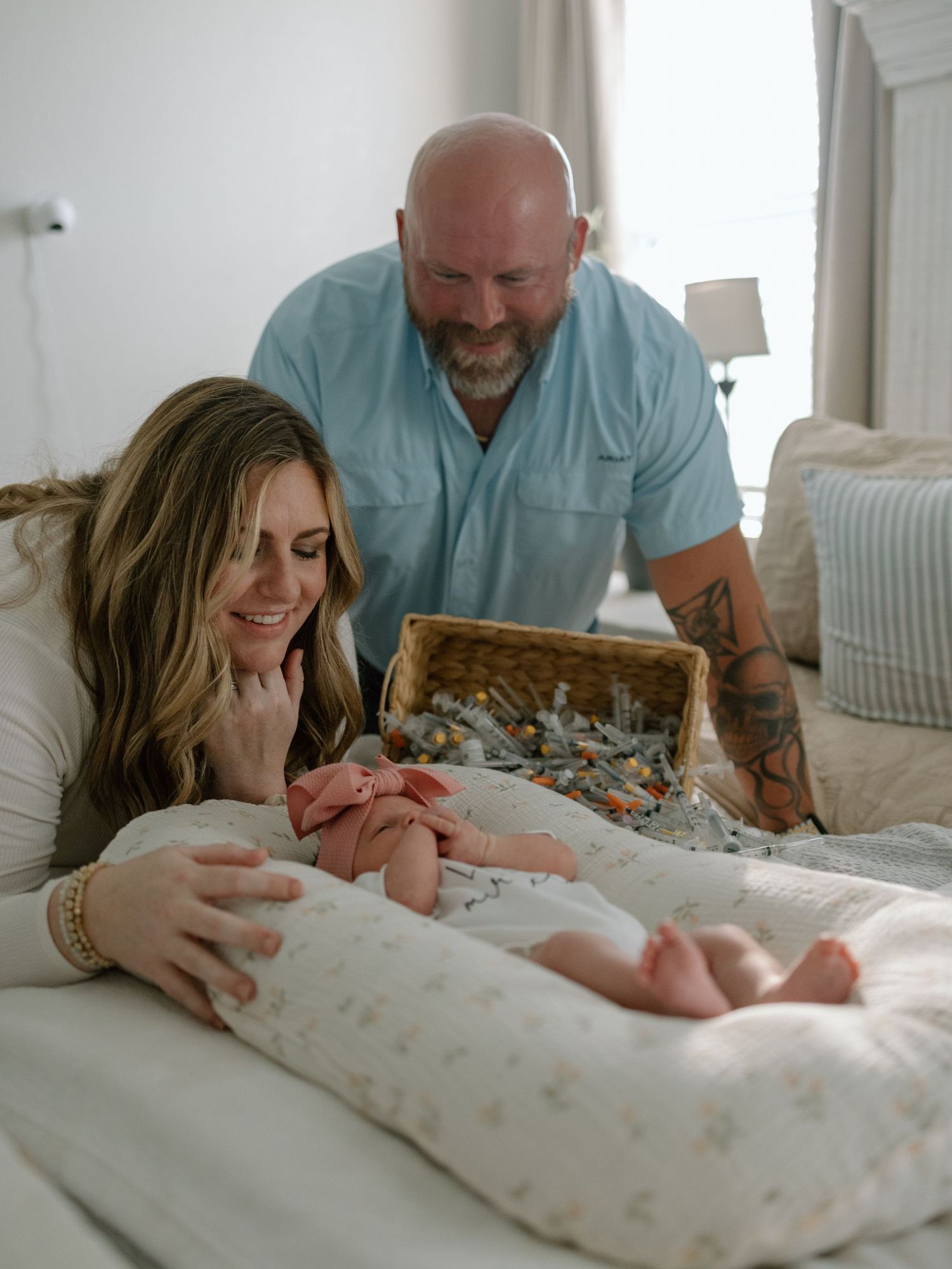 Parents lovingly admiring their newborn baby on a bedding dock in a bright, cozy bedroom setting.