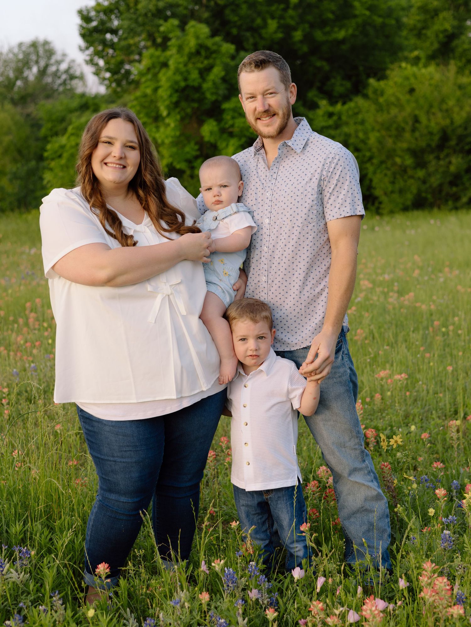 A family stands together in a wildflower meadow on a sunny spring day wearing coordinated casual outfits.