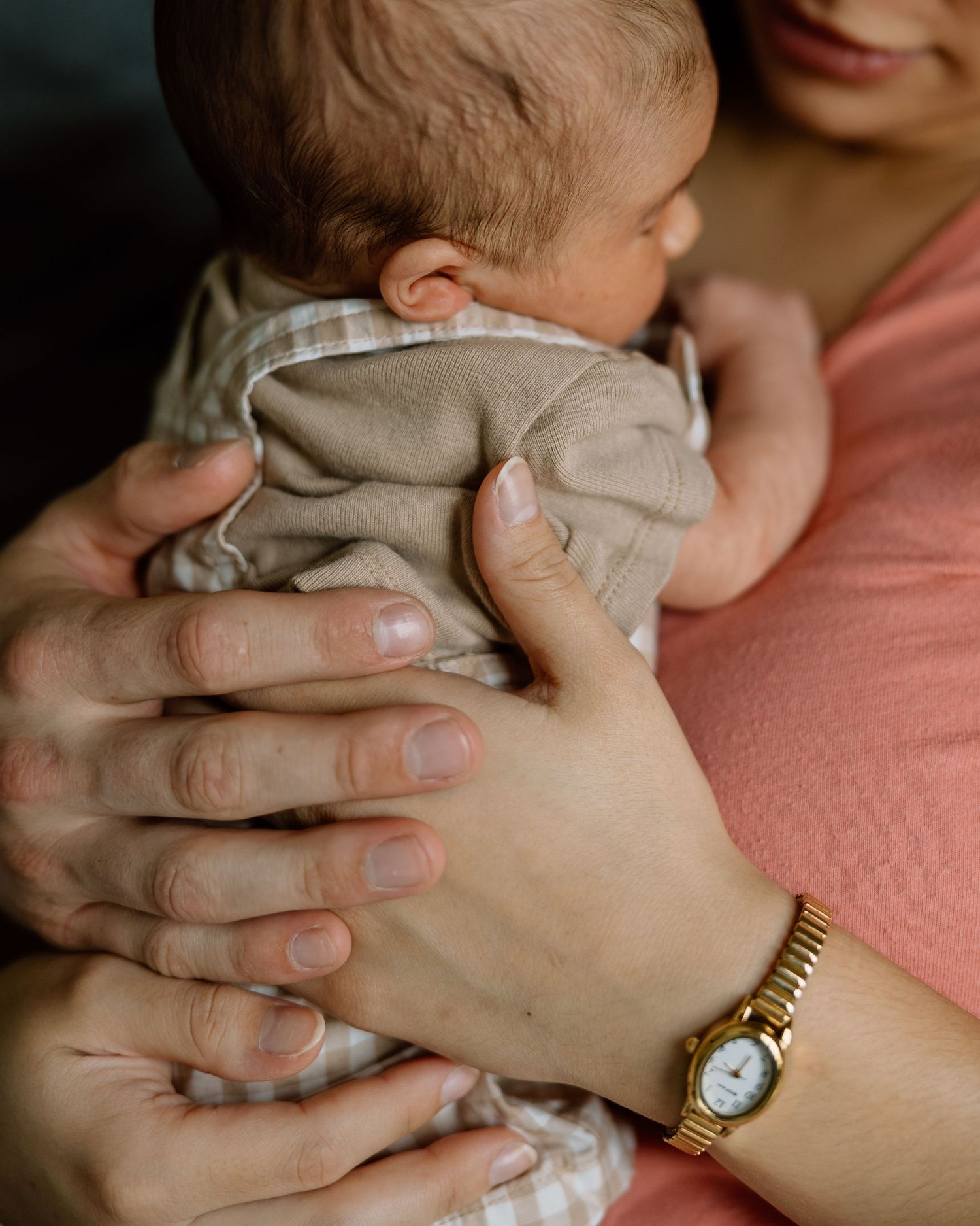 Close-up of parents hands gently holding a newborn baby wearing a plaid onesie.