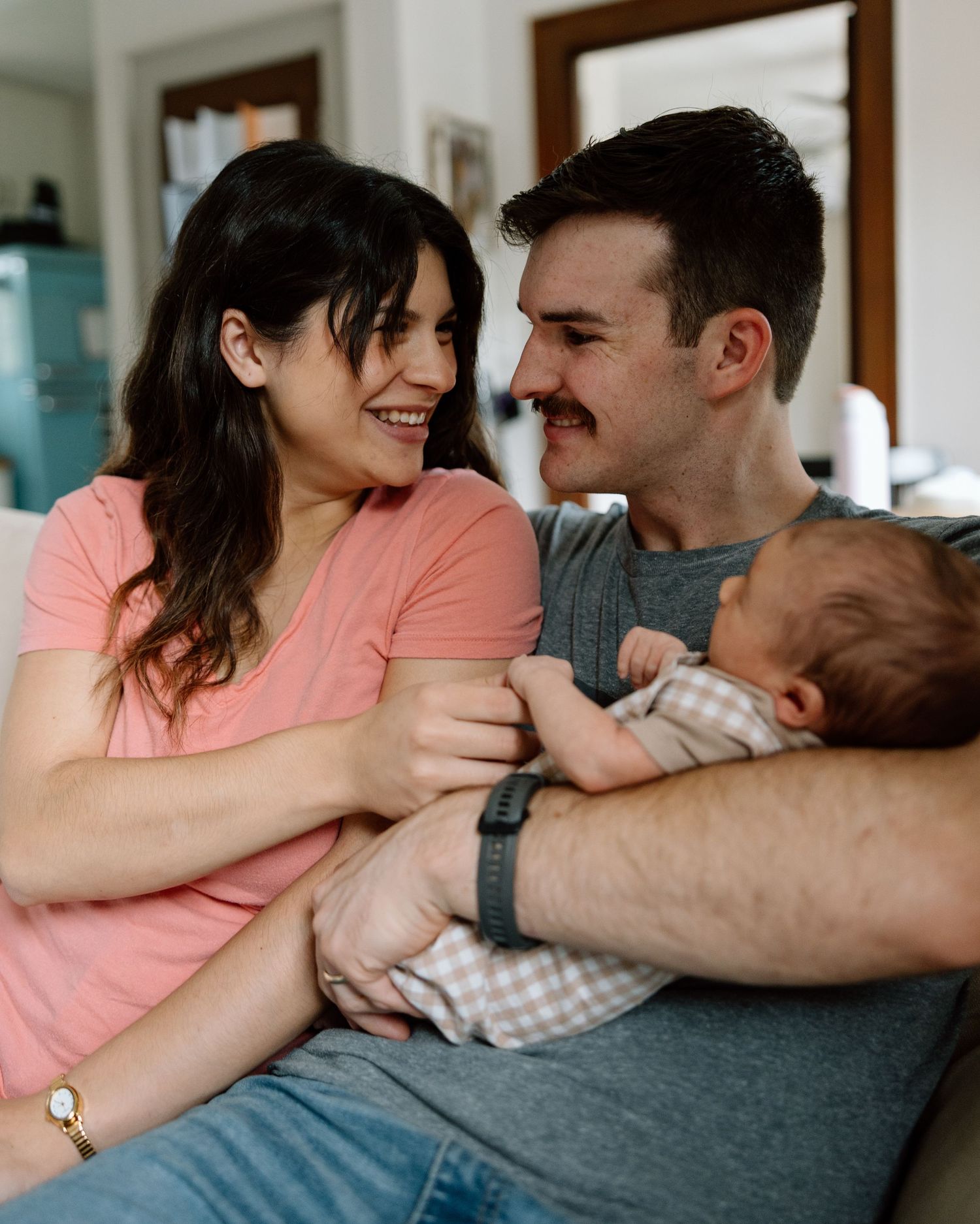 Smiling couple holding their newborn baby together in a cozy home setting.