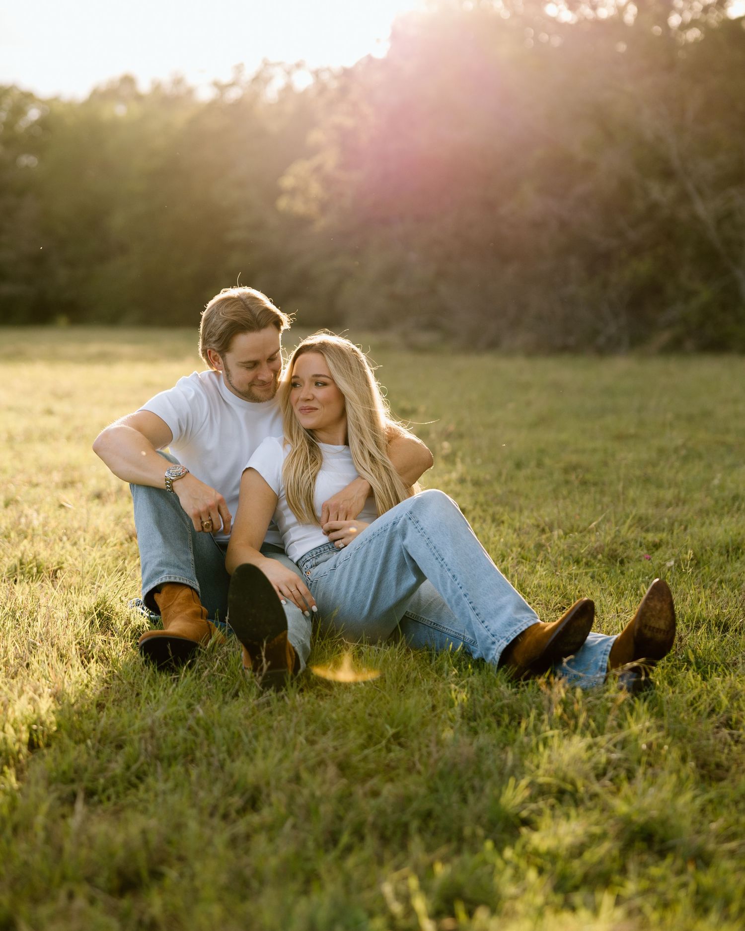 Couple sitting together in golden sunset light on green grass, sharing a tender quiet moment.