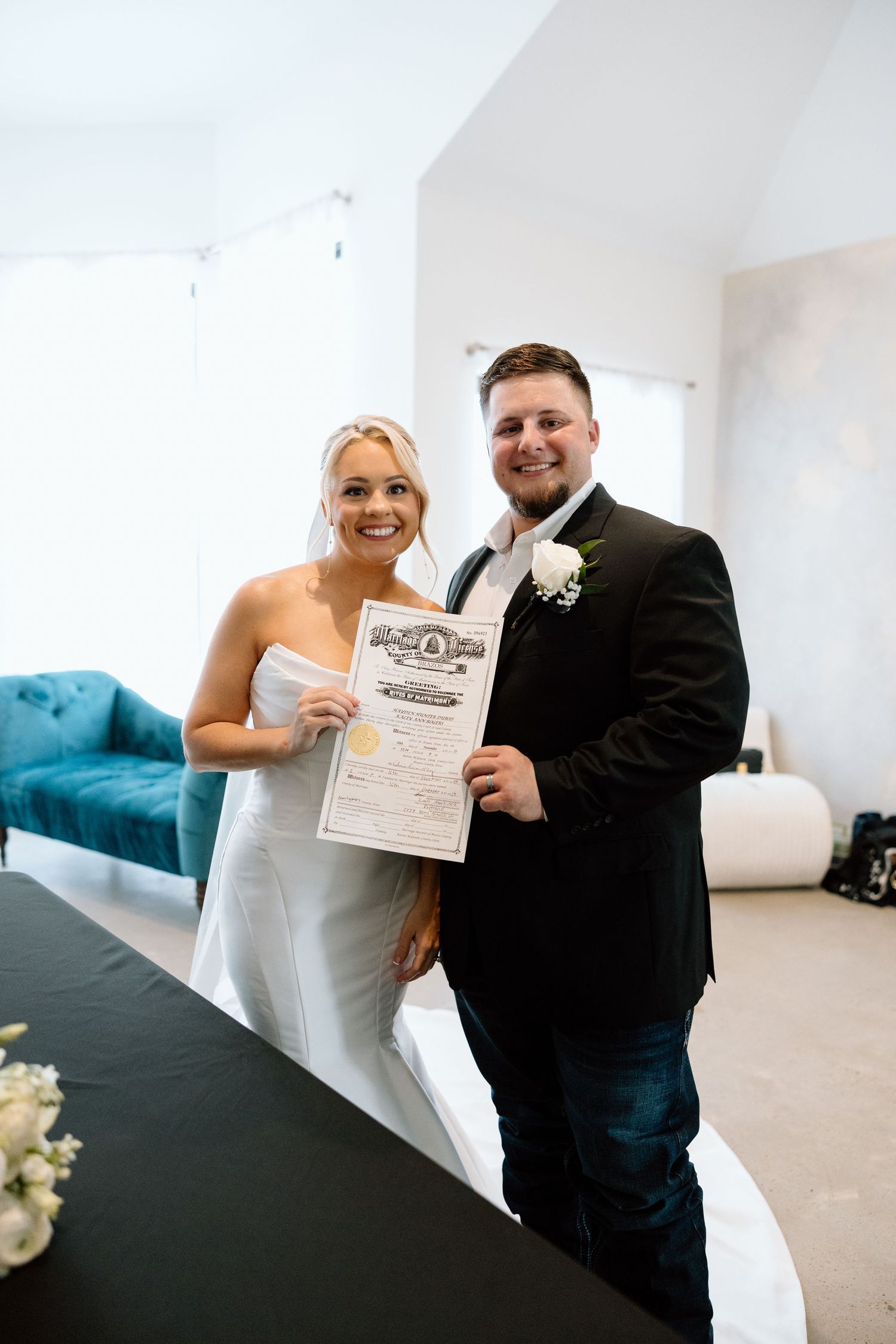 Newlyweds smile while holding their marriage certificate after signing at wedding venue.