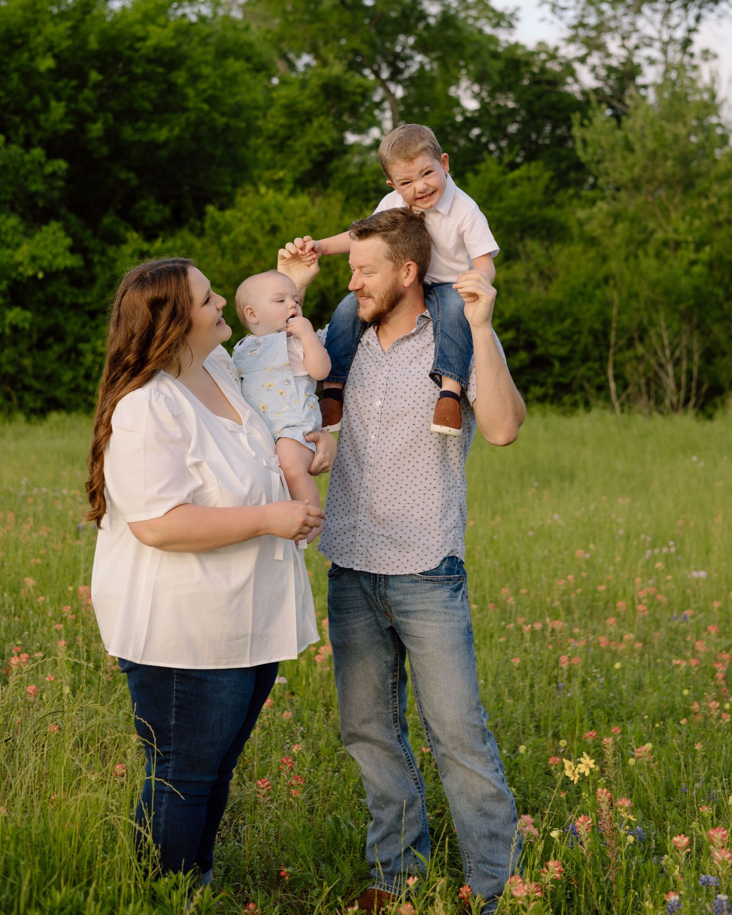 Happy family of four stands together in a wildflower meadow at sunset during outdoor photo session.